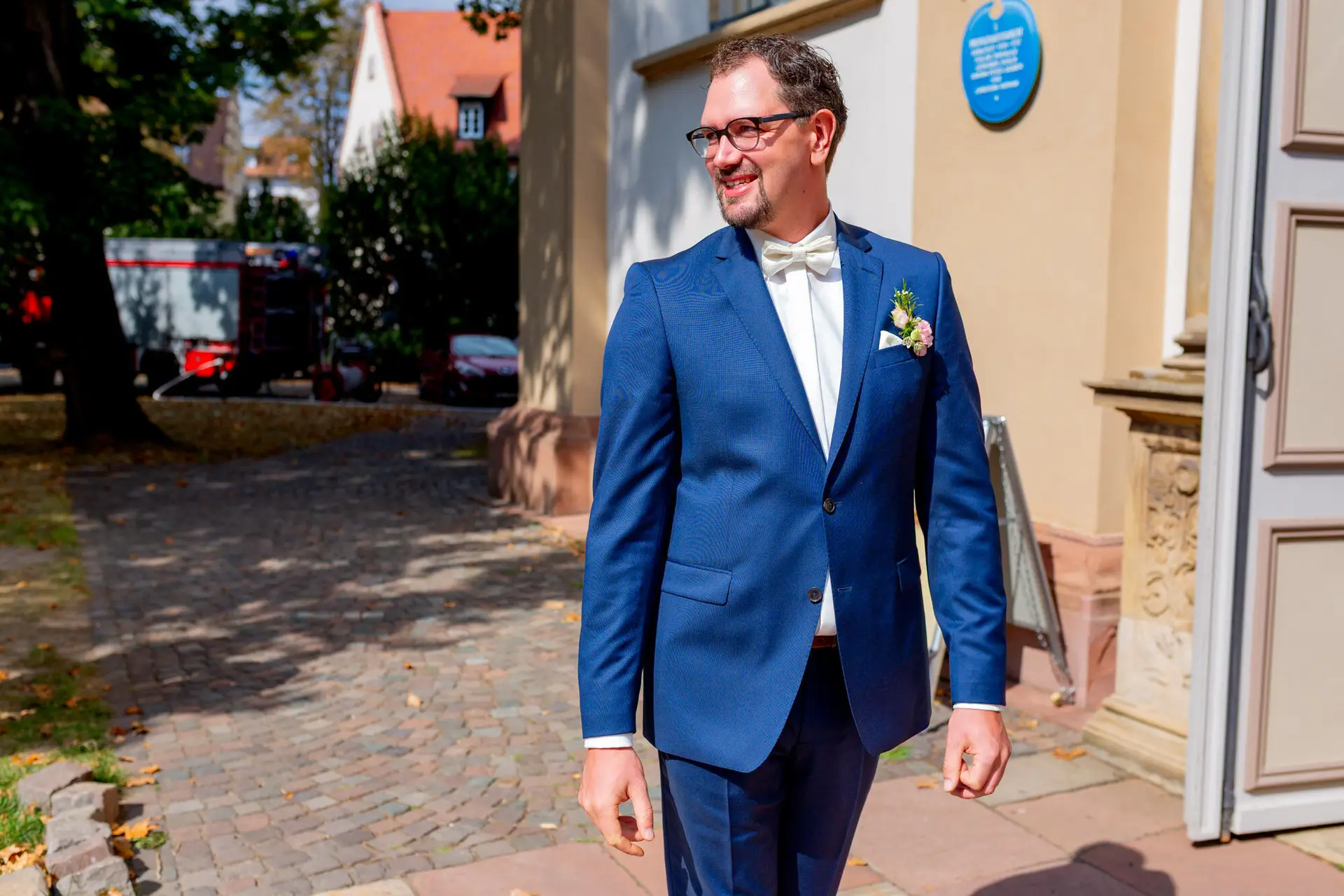 Brautpaar im eleganten Marineblau vor dem Kirchenportal bei sonnigem Wetter