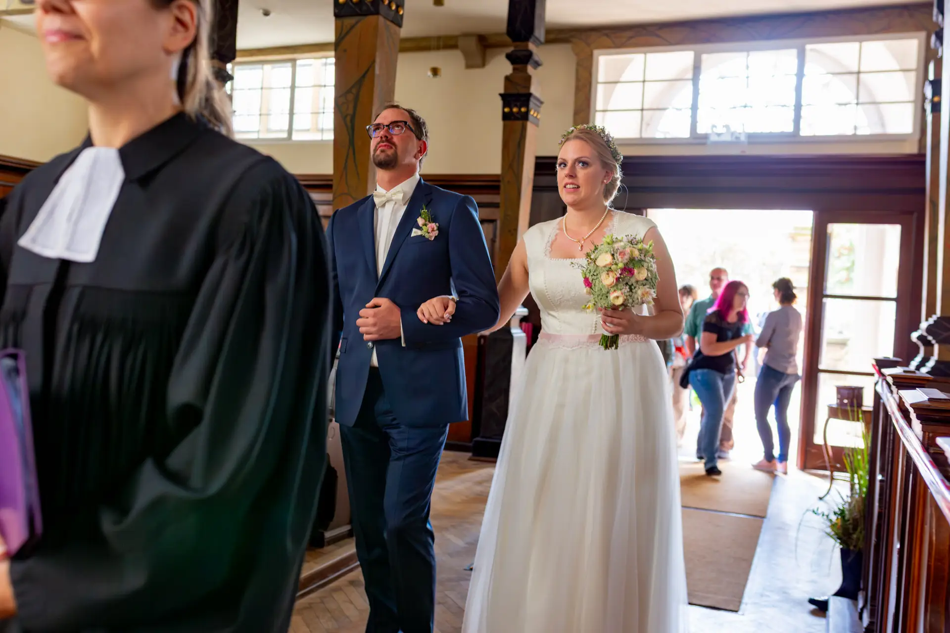 Brautpaar geht zur Kirche, umgeben von Holzbalken und Blumen