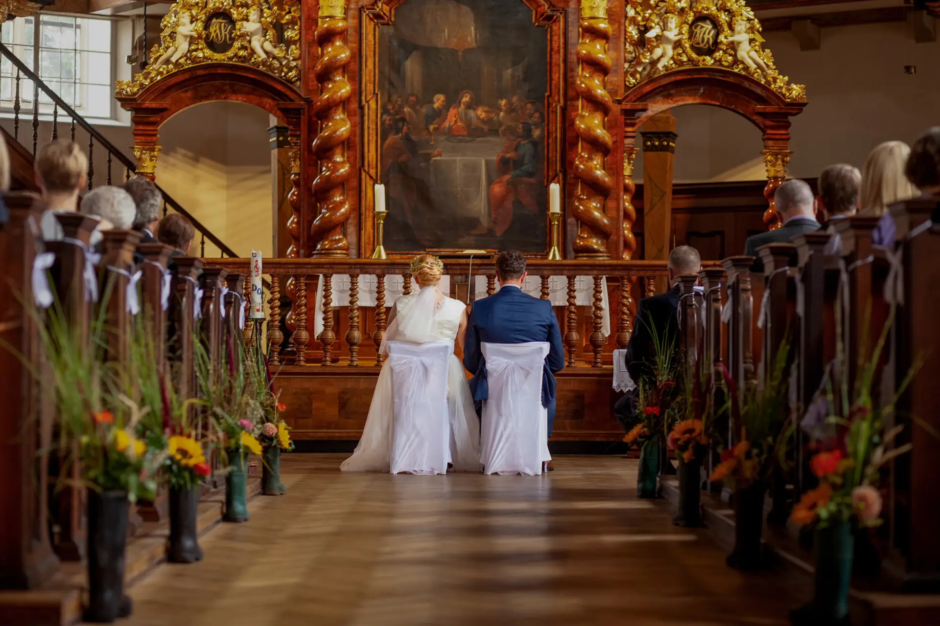 Brautpaar kniet am Altar einer Kirche mit Blumendekoration und Kirchenfenstern