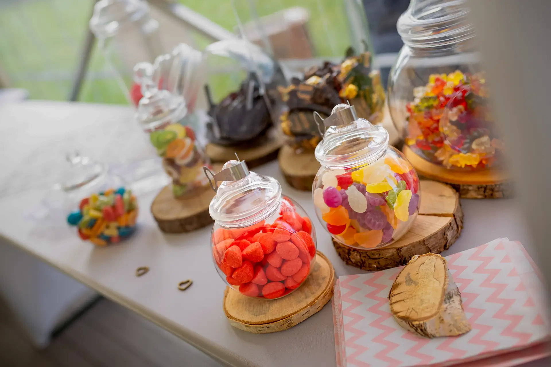 Gläser mit bunten Süßigkeiten, Holzscheiben und Hochzeitstorte auf weißem Tisch