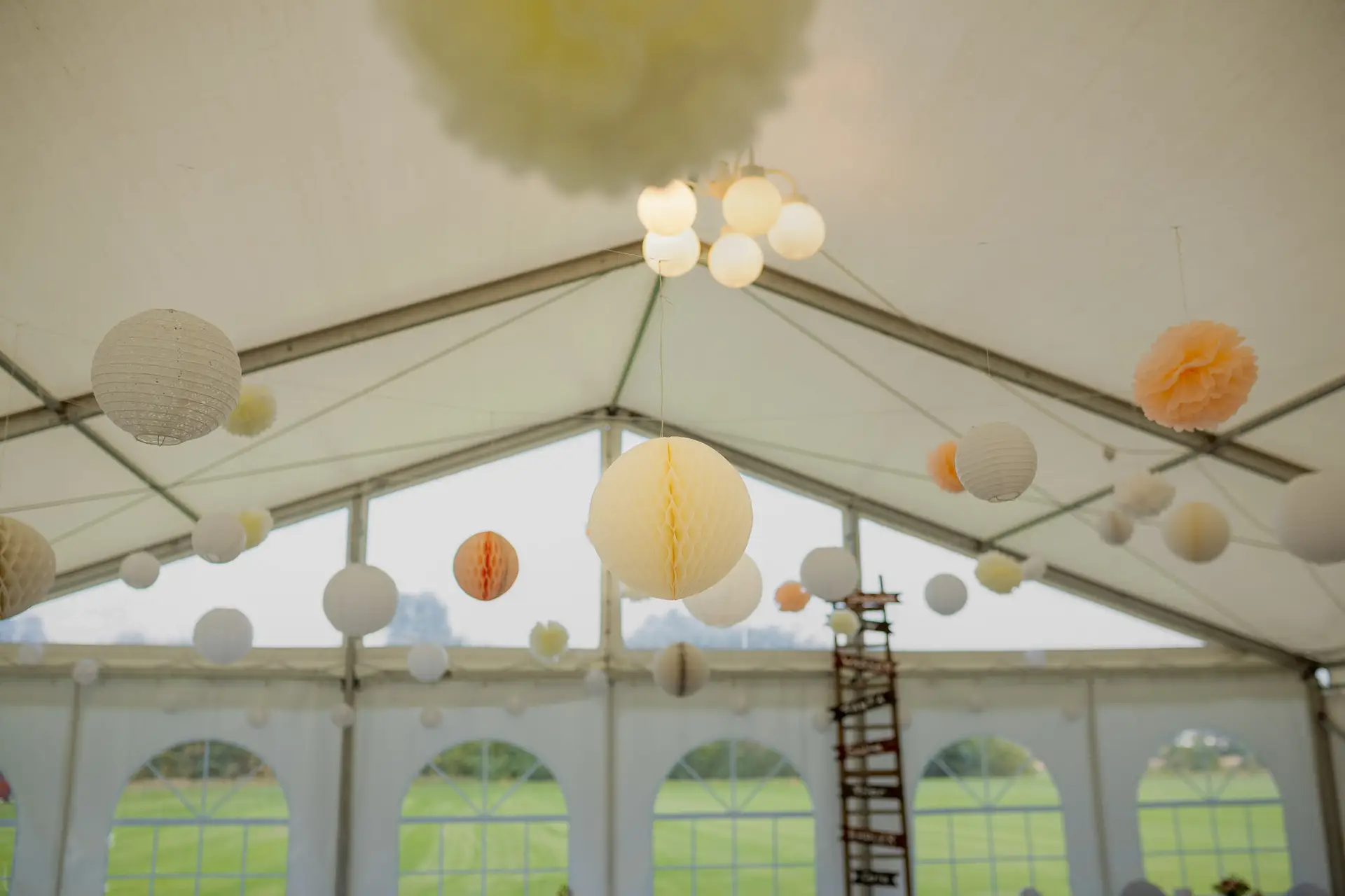 Weiße Laternen hängen an den Zeltstangen beim Hochzeitsfest im Grünen