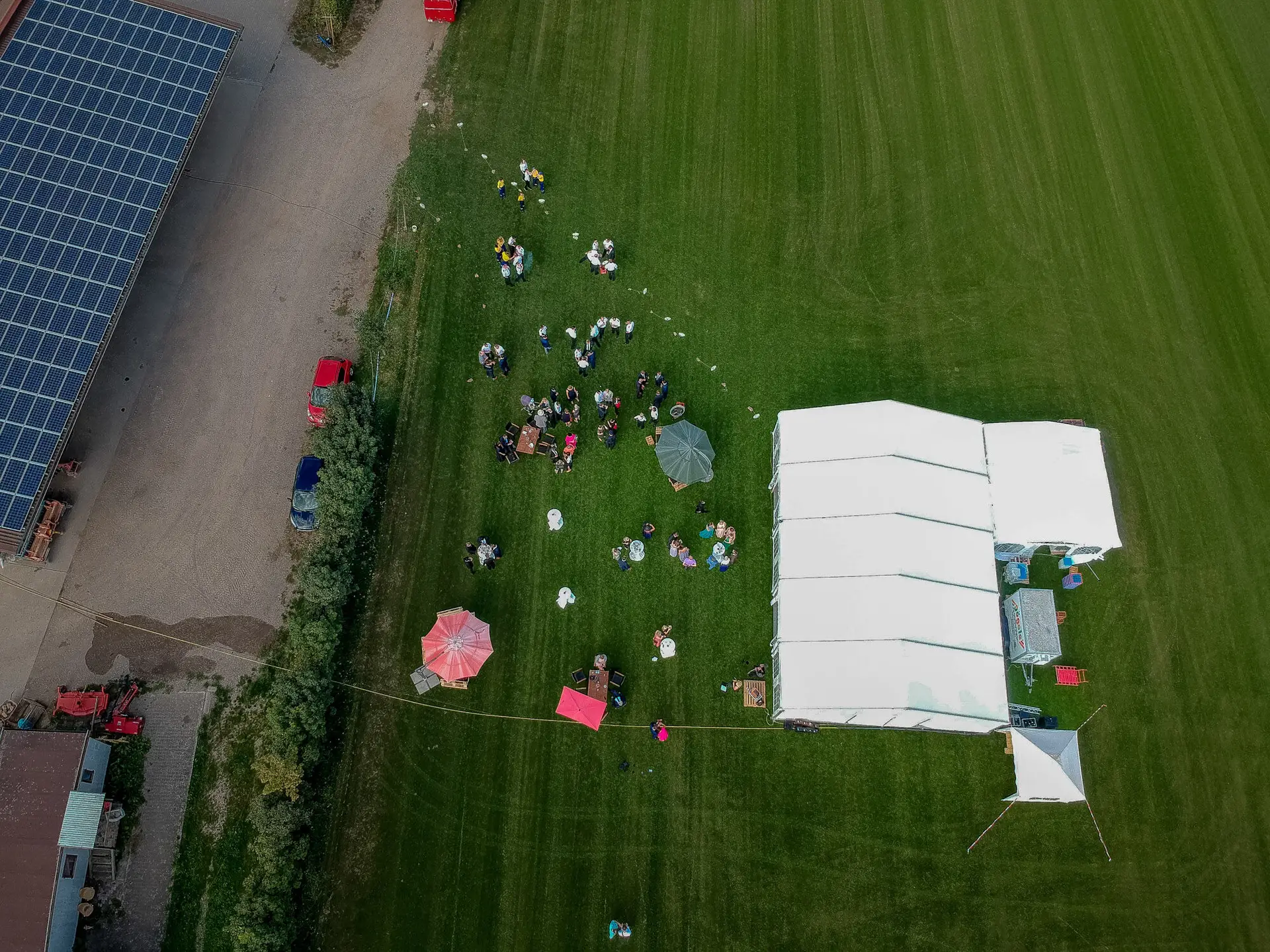 Drohnenaufnahme: Hochzeitsgesellschaft unter weißem Festzelt auf grüner Wiese in Reilingen