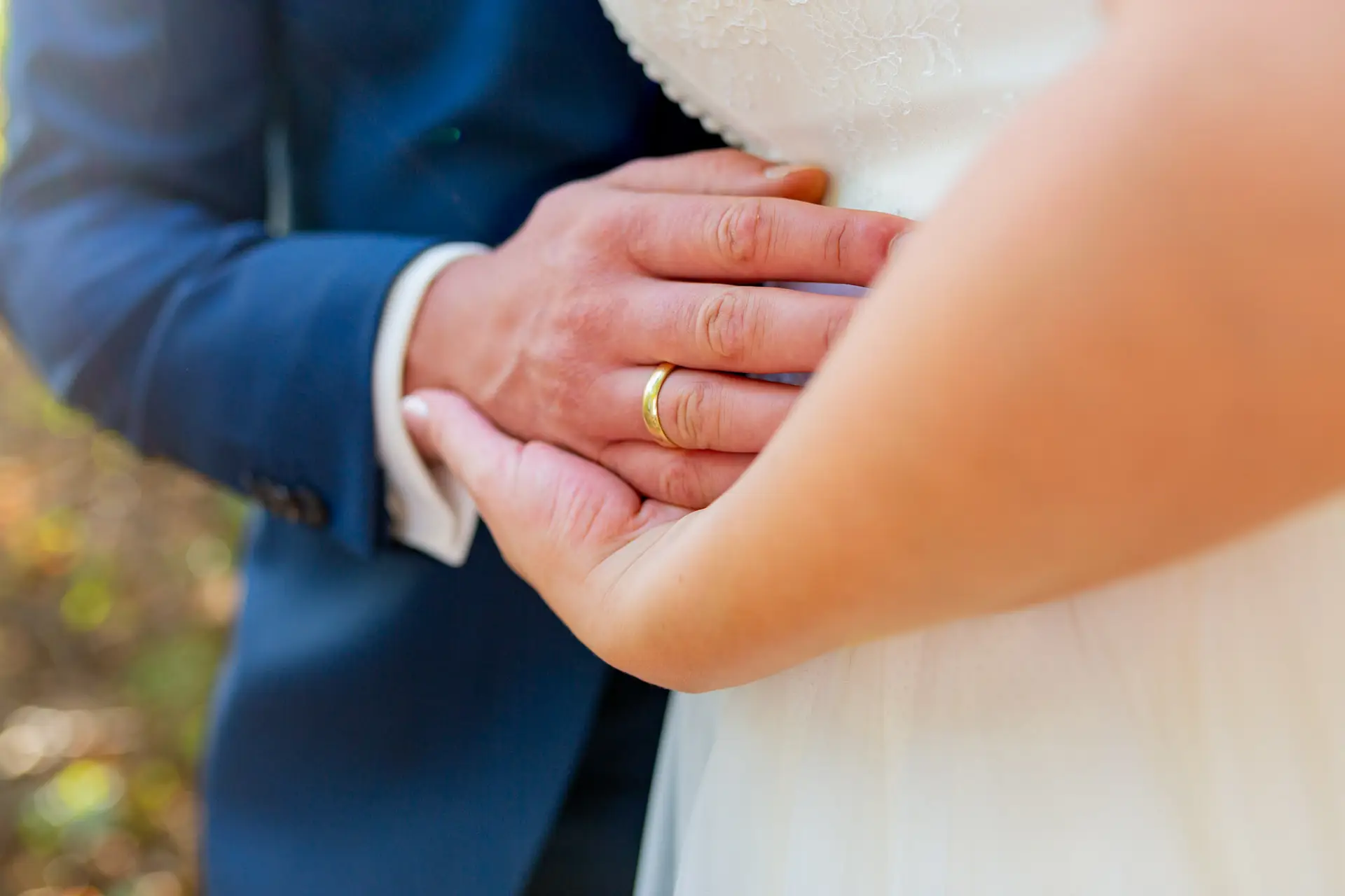 Brautpaar hält Hände – Eheringe glänzen im Sommerlicht am See