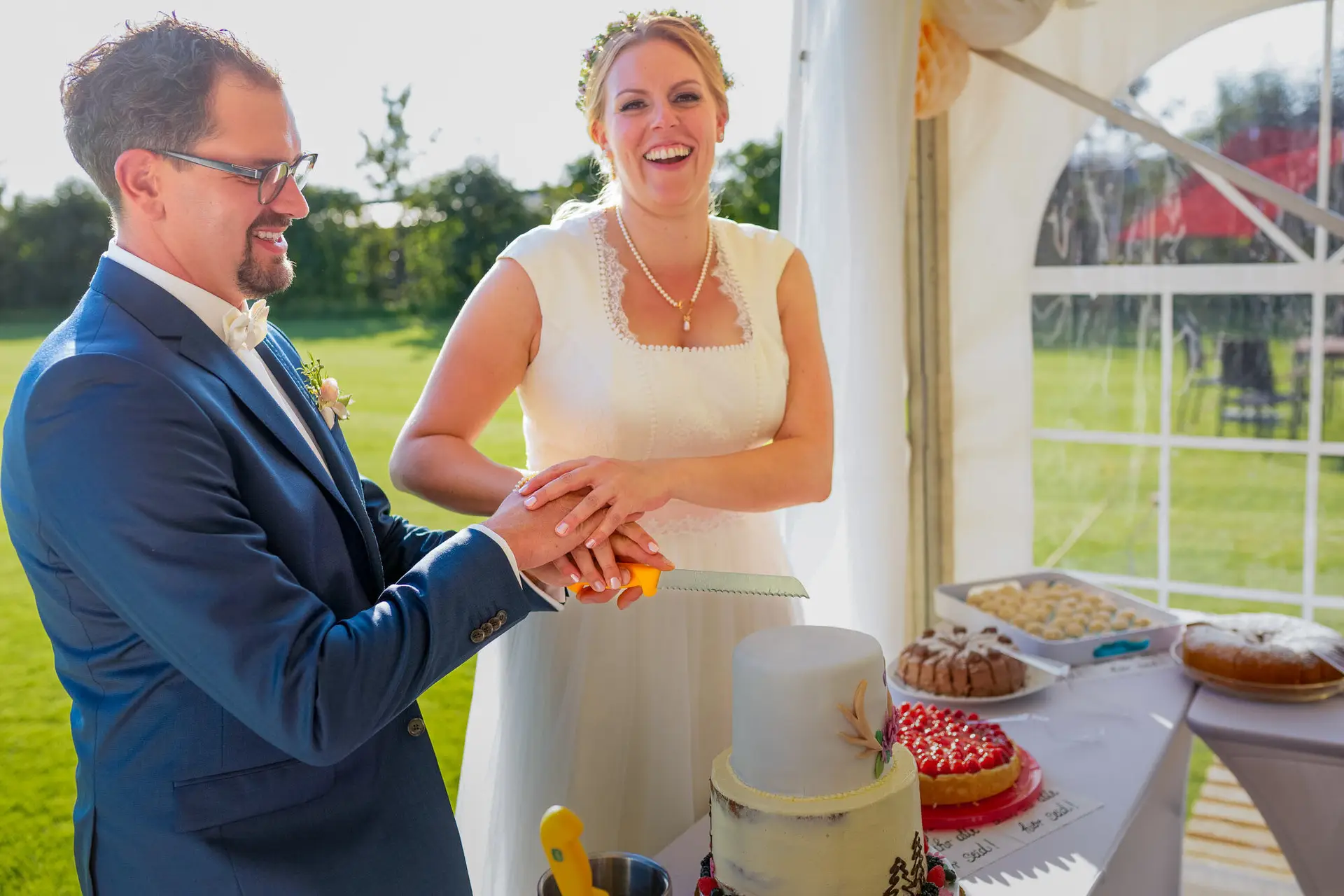 Brautpaar schneidet gemeinsam die Hochzeitstorte auf der grünen Wiese