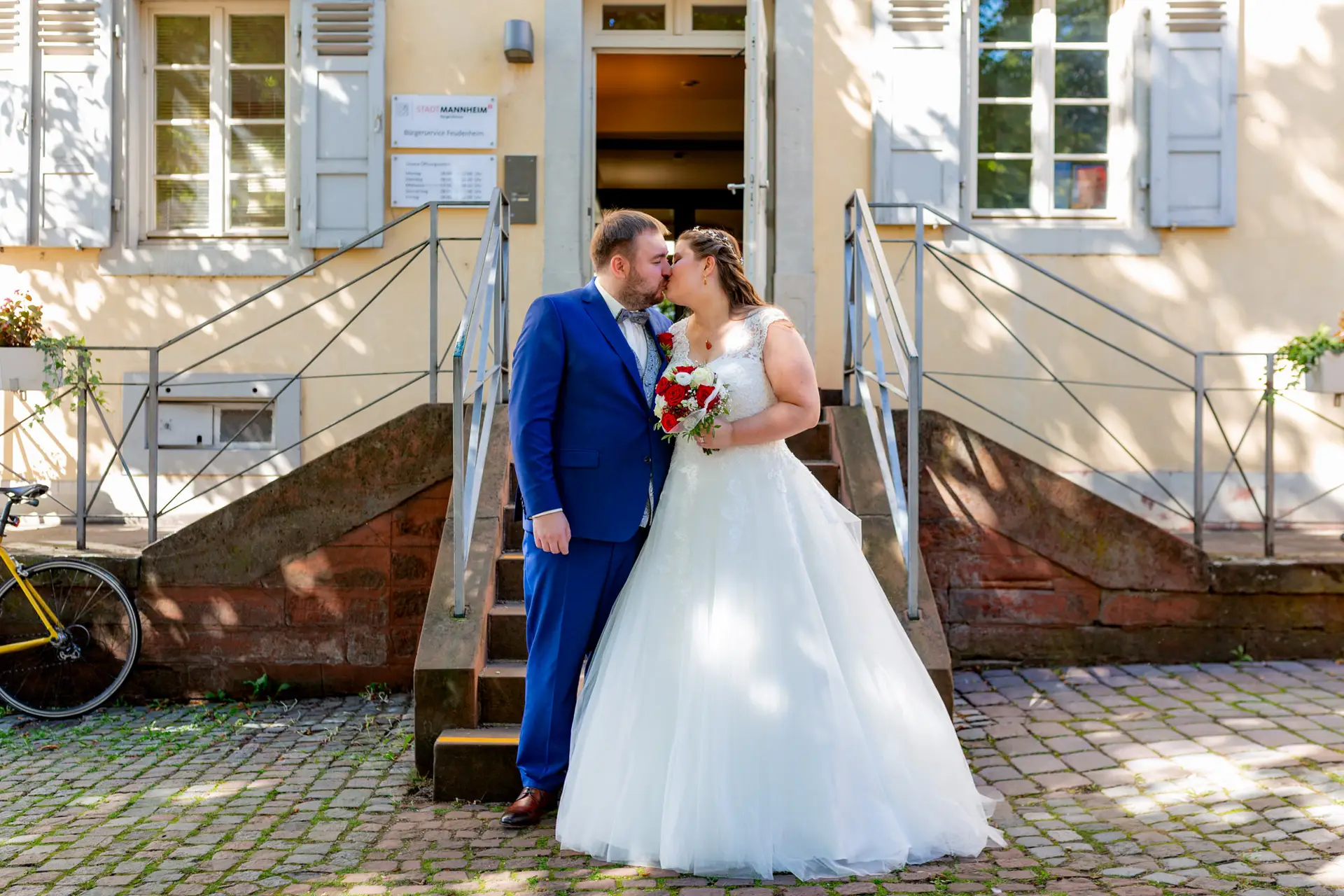 Brautpaar steht auf der Steintreppe vor dem Standesamt mit Brautstrauß und Fahrrad im Hintergrund