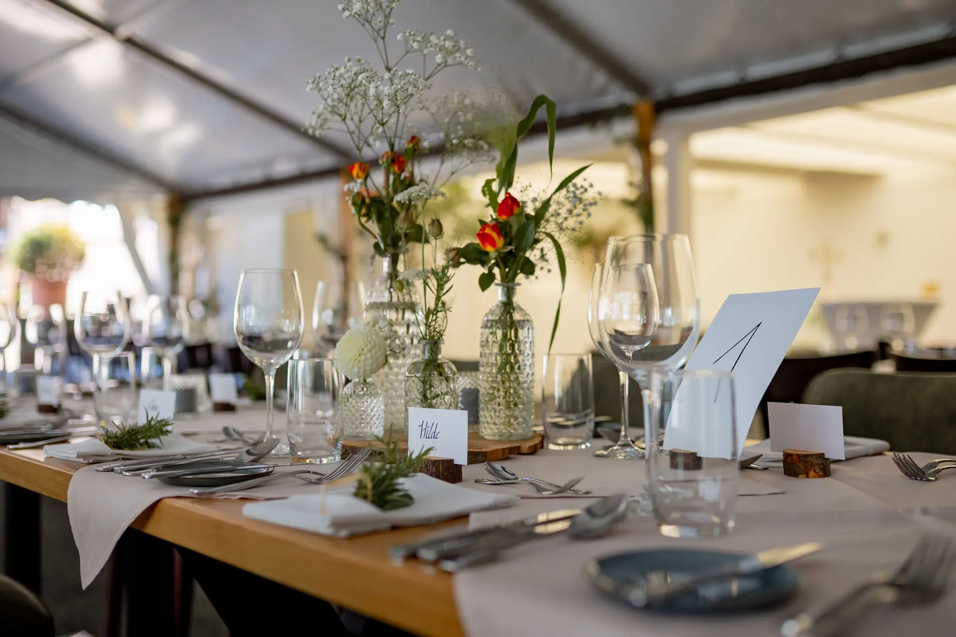 Runder Hochzeitstisch im Zelt mit floraler Tischdekoration und Namensschildern für die Gäste