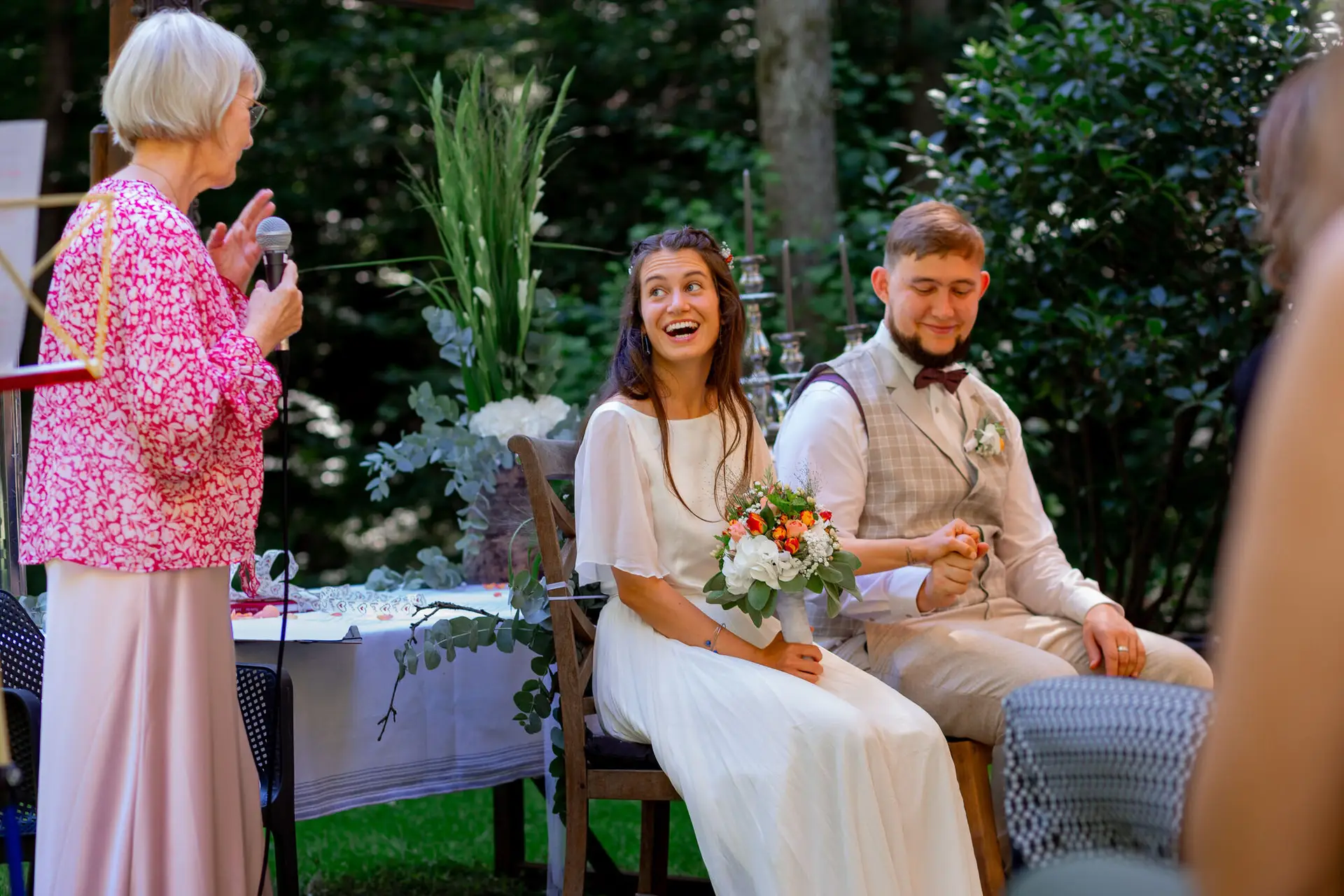 Traurednerin mit Mikrofon hält ihre persönliche Ansprache, Brautpaar hört aufmerksam zu