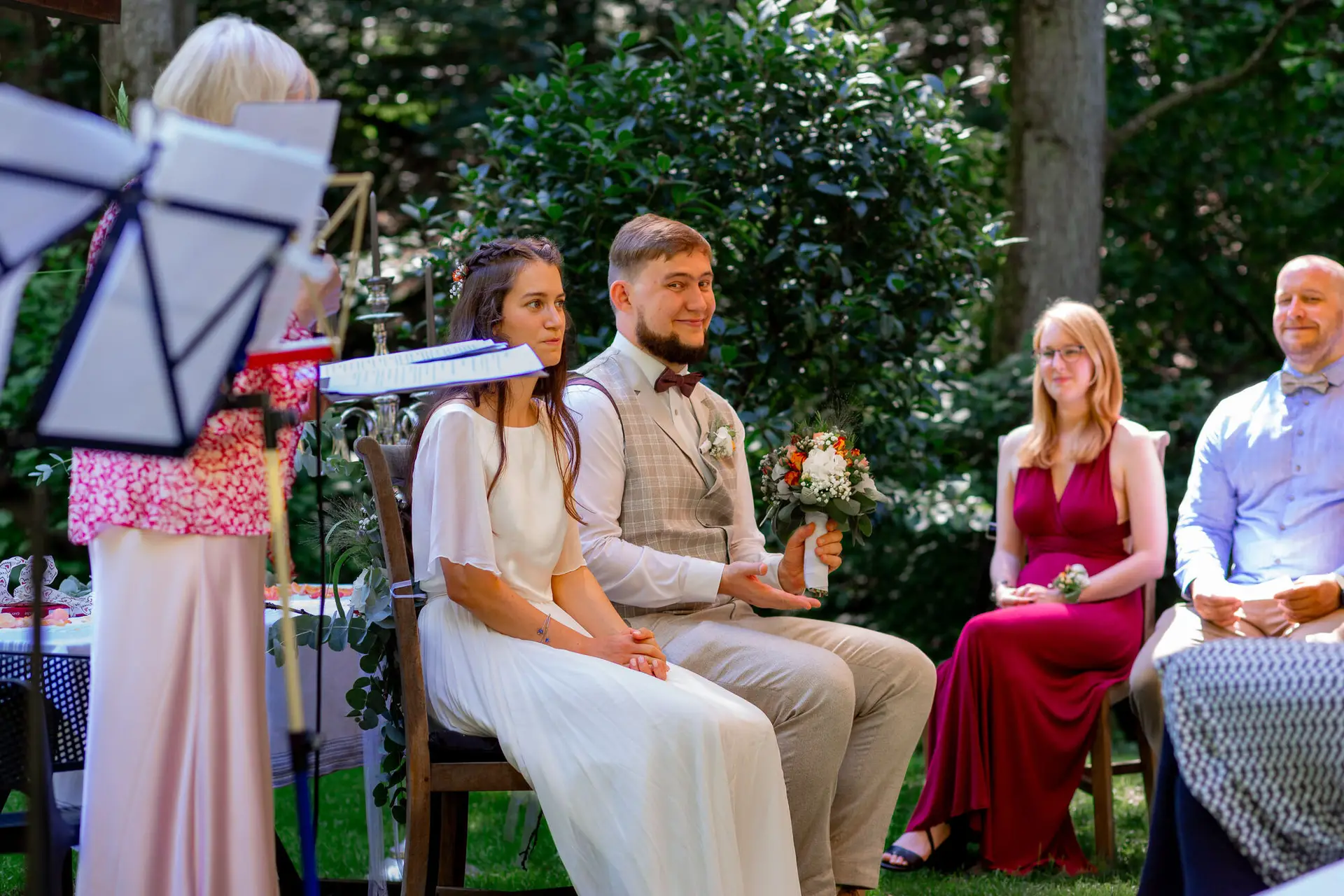 Brautpaar auf Stühlen vor dem Gartenaltar, musikalische Begleitung im Hintergrund