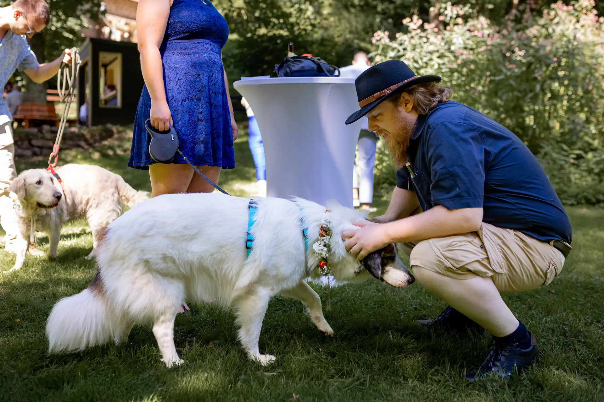 Gast bückt sich hinunter zum weißen Retriever mit Blumenkrone beim fröhlichen Empfang