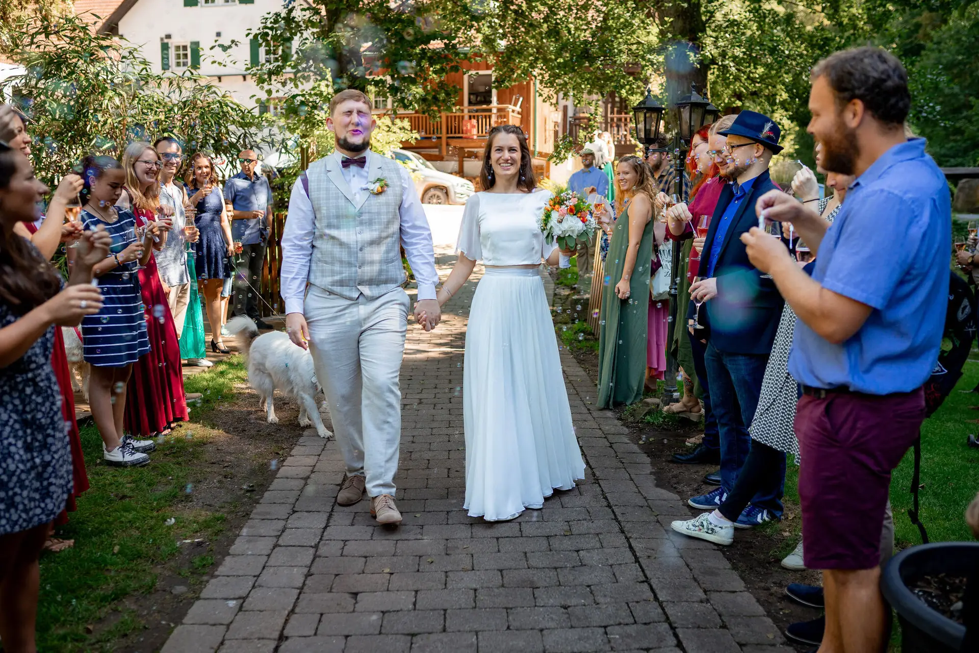 Brautpaar schreitet Arm in Arm durch die jubelnden Gäste mit Seifenblasen, Sommer-Atmosphäre pur