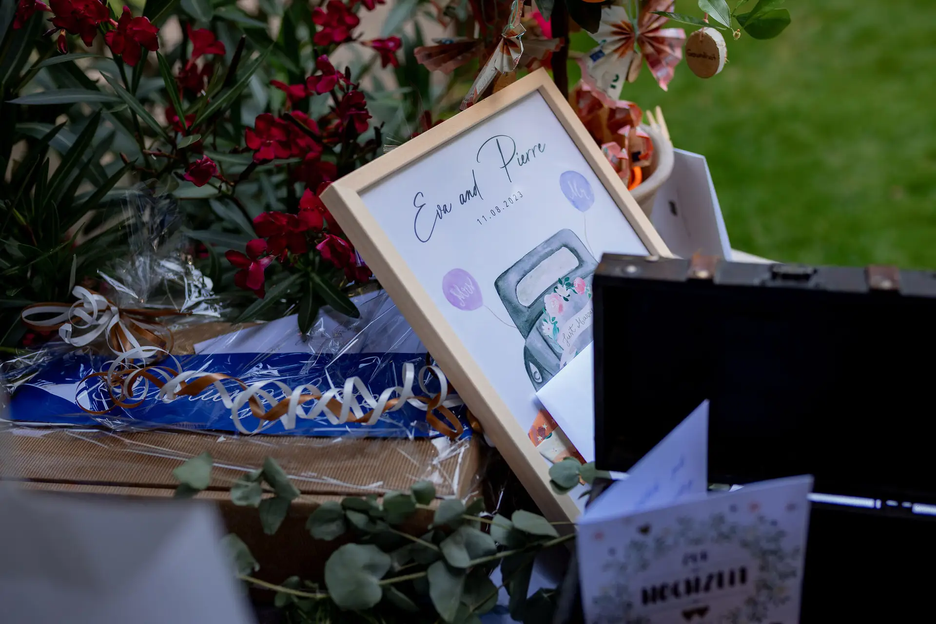 Holzschild "Eva und Pierre" mit Hochzeitsdatum, Blumenstrauß und Koffer auf dem Empfangstisch