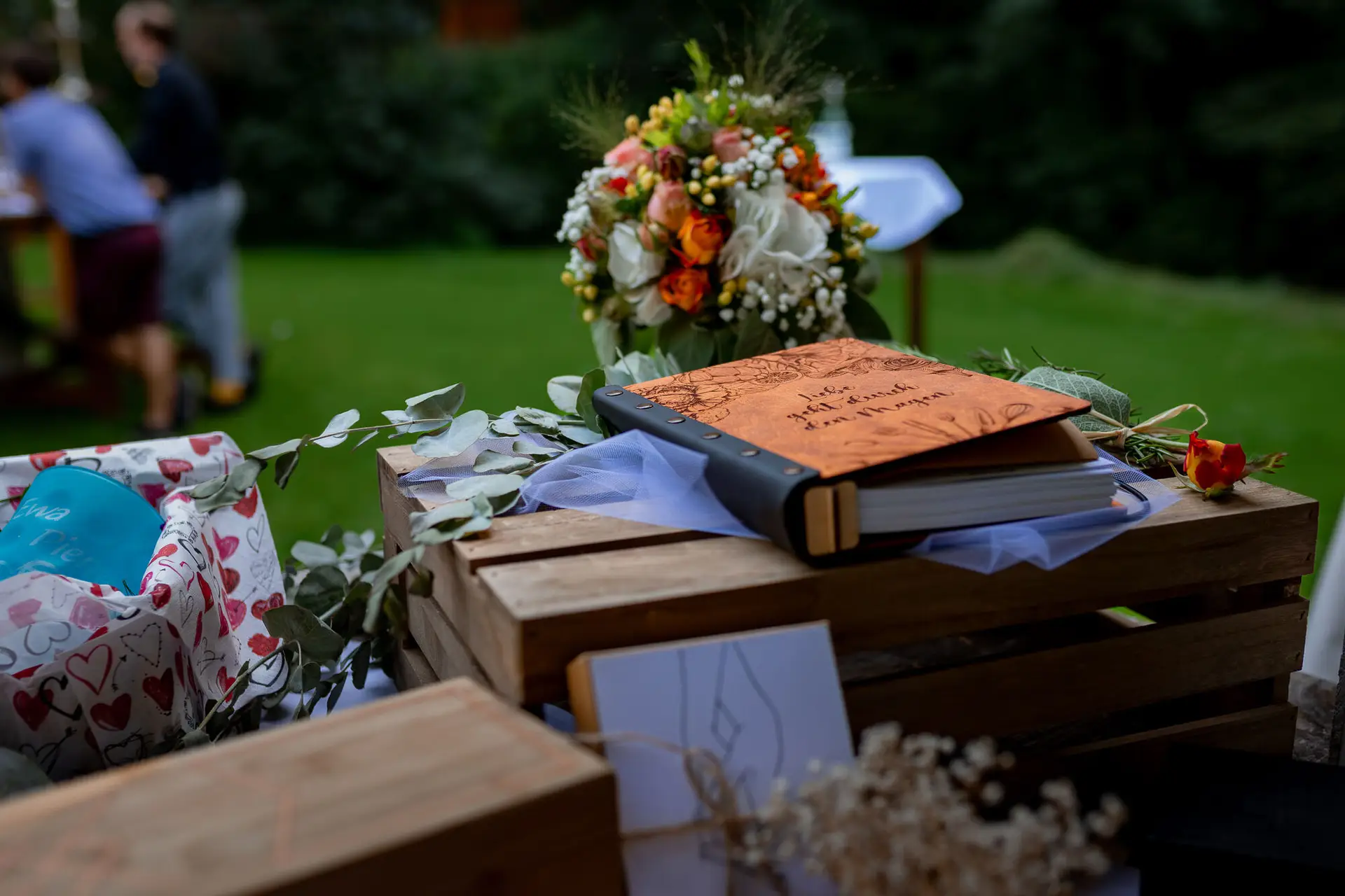 Rustikales Holzbord mit persönlichem Gästebuch und Blumenkrone als Deko-Arrangement