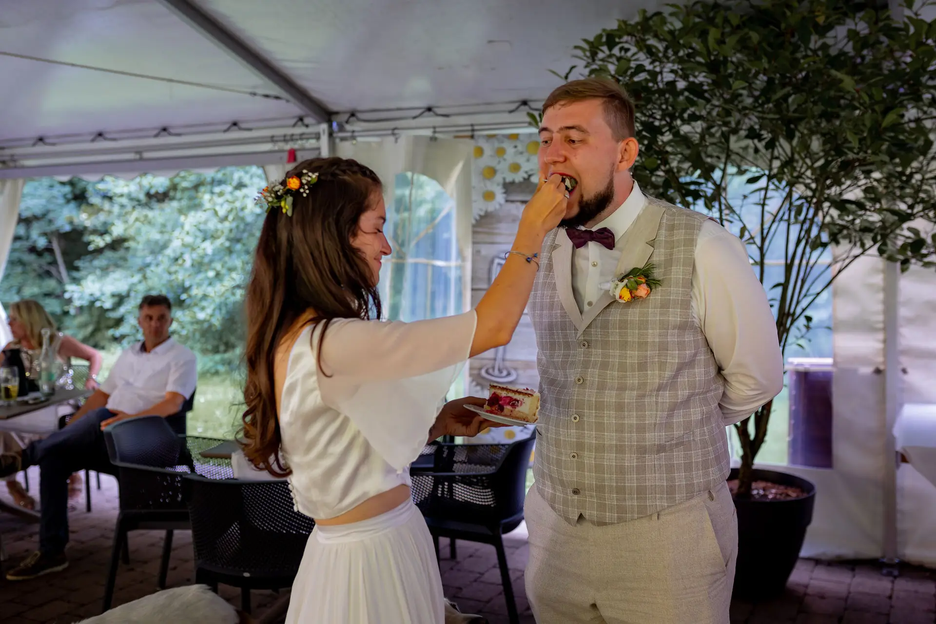 Bräutigam lacht herzlich, als Braut ihm spaßhaft ein Tortenstück ins Gesicht drückt
