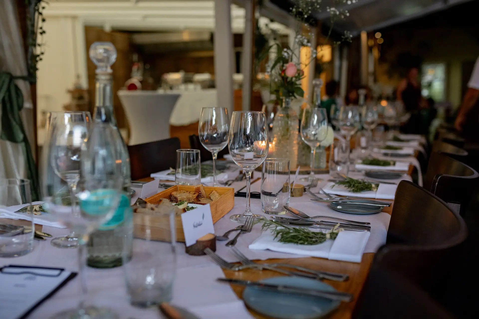 Romantisch gedeckter Abendtisch mit Blumenarrangements und Kerzenlicht, Gäste im Hintergrund