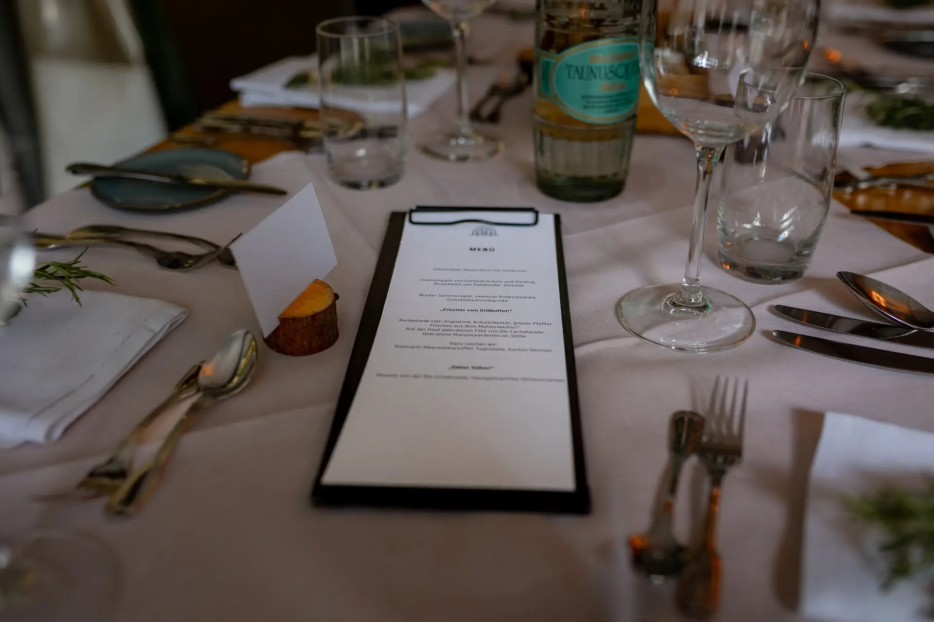 Tischdetail des Hochzeitsabendessens: Menükarte, Weinflasche und persönliche Dekoration