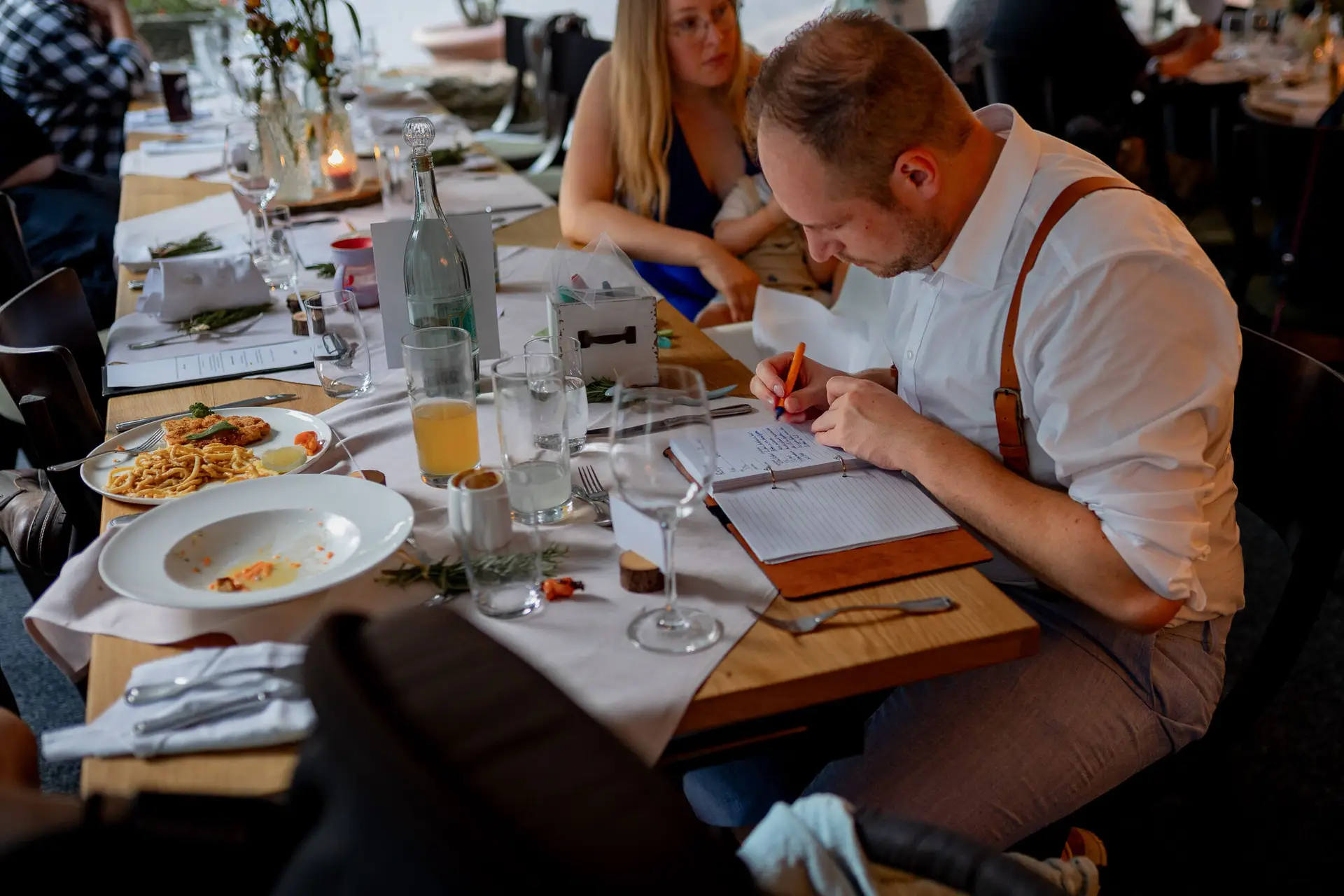 Hochzeitsspiel beim Abendessen: Gast schreibt ins Notizbuch bei Pasta und Wein