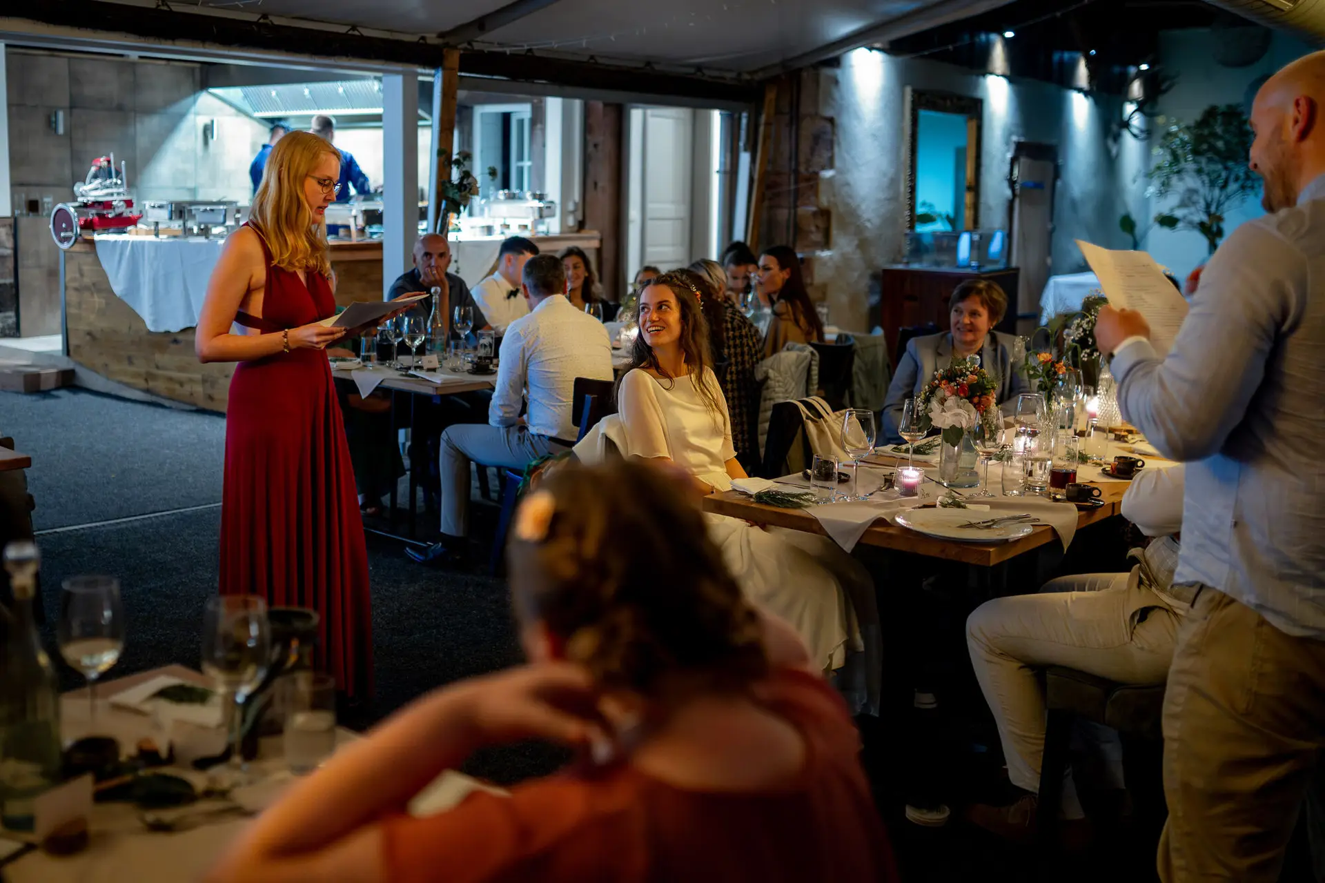 Brautjungfer in Rot hält eine herzliche Ansprache, Gäste hören aufmerksam zu