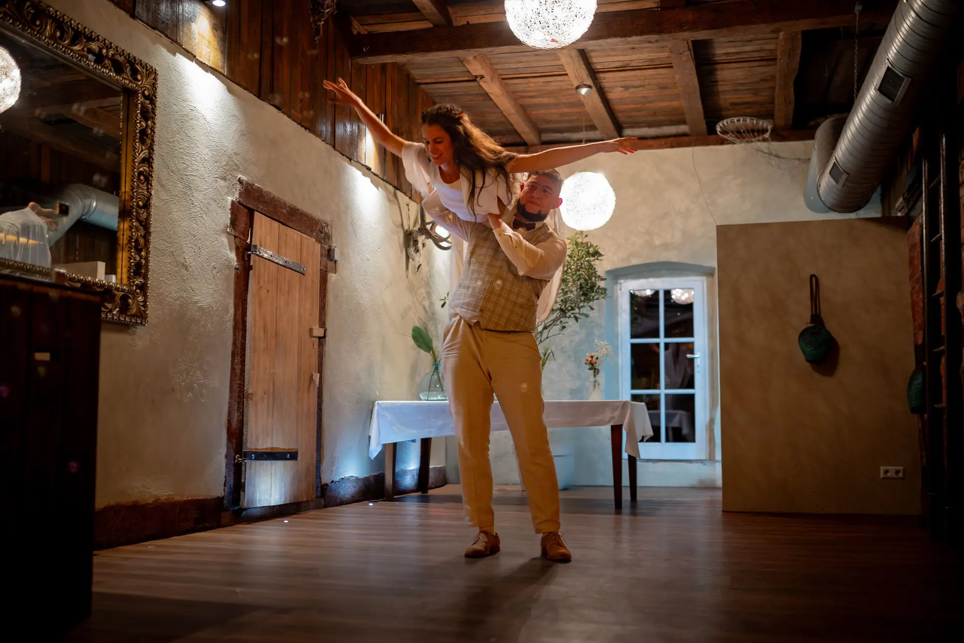 Bräutigam trägt die Braut tanzend durch den rustikalen Holzraum der Feierlocation
