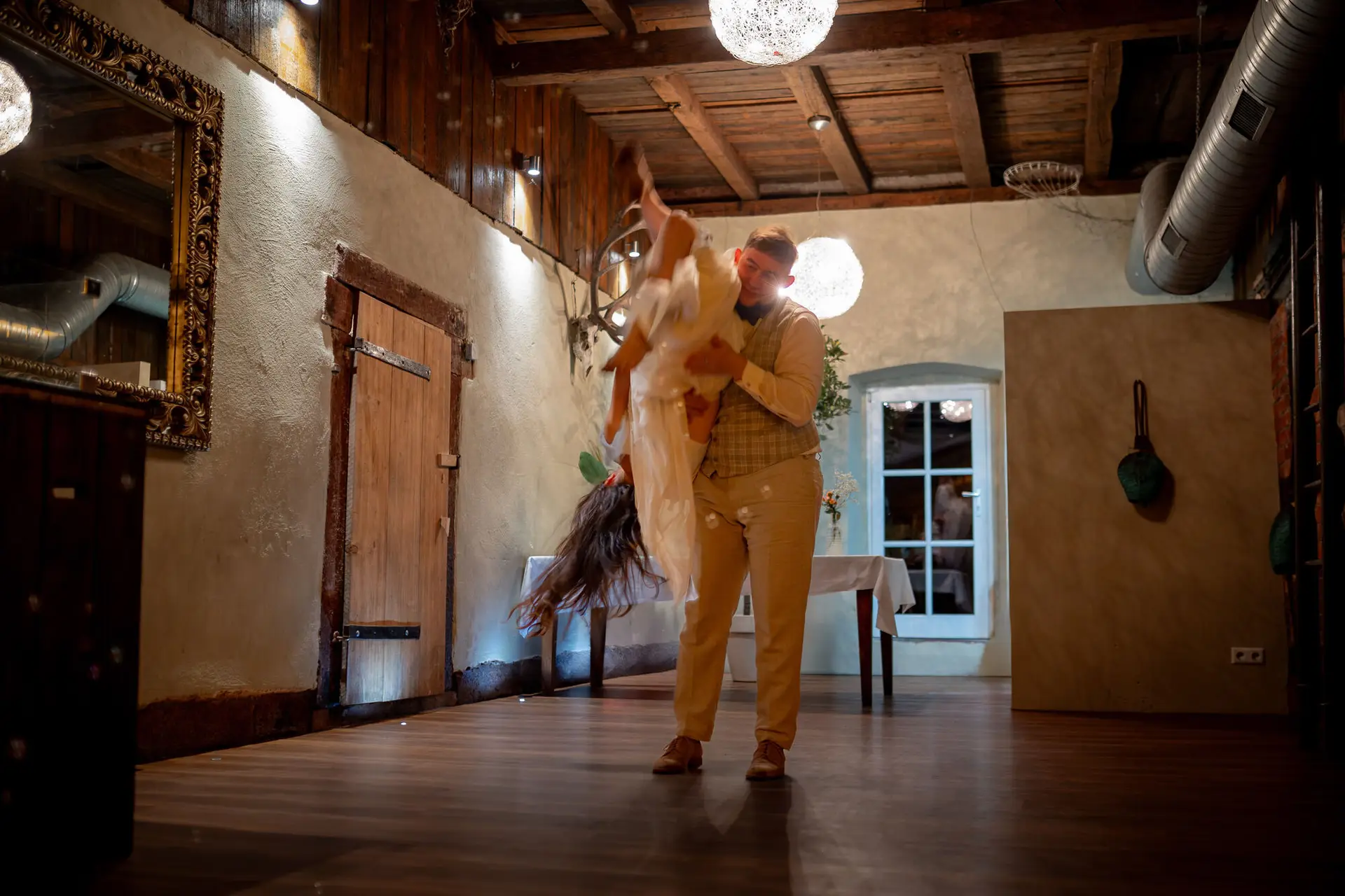 Bräutigam dreht die Braut im Walzer unter den Hängeleuchten des Holzsaals der Mühle