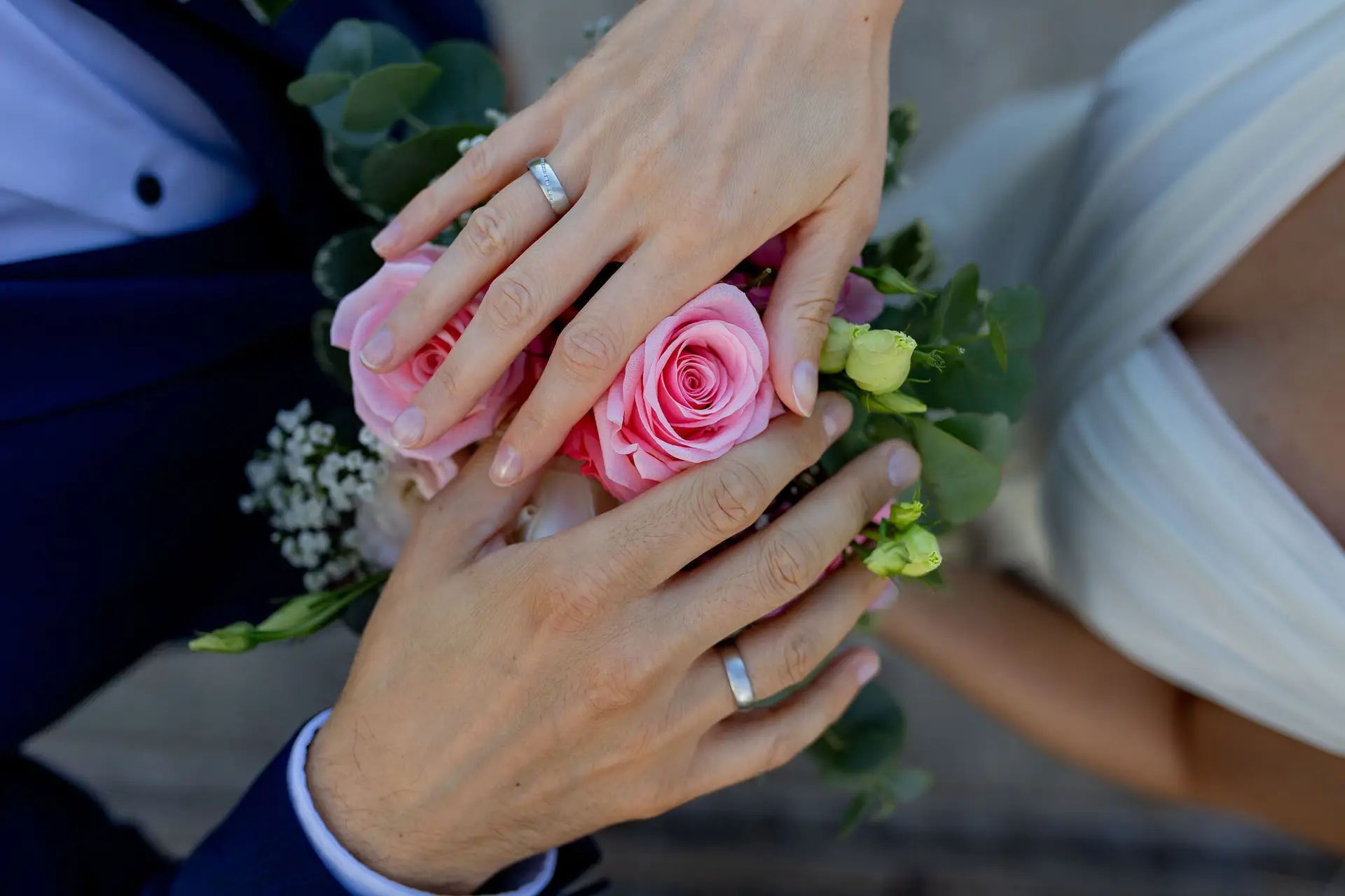 Nahaufnahme der Hände des Brautpaares mit Ehering und einer rosa Rose