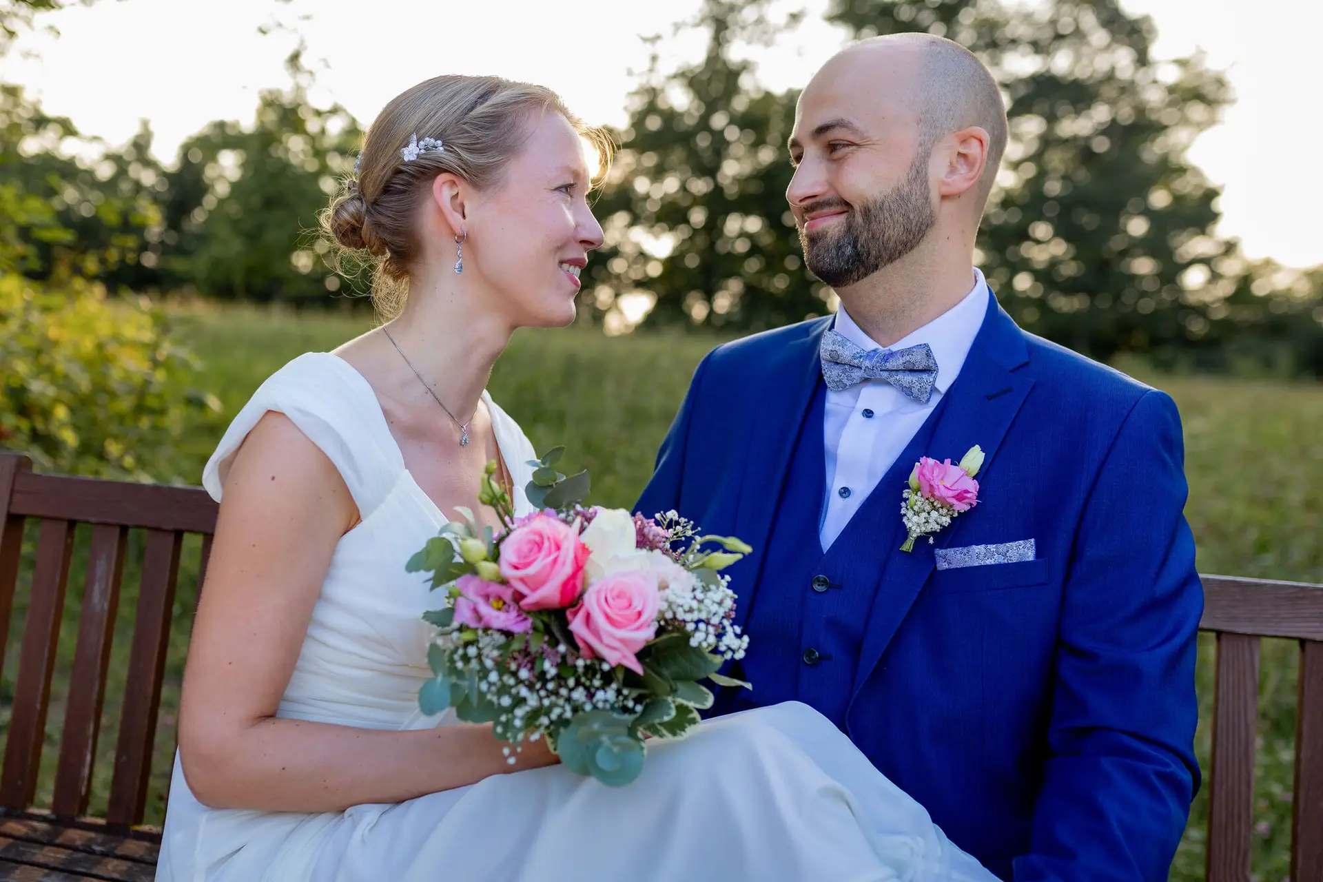 Brautpaar sitzt lächelnd auf einer Holzbank auf einer Wiese im Schlossgarten Herrnsheim