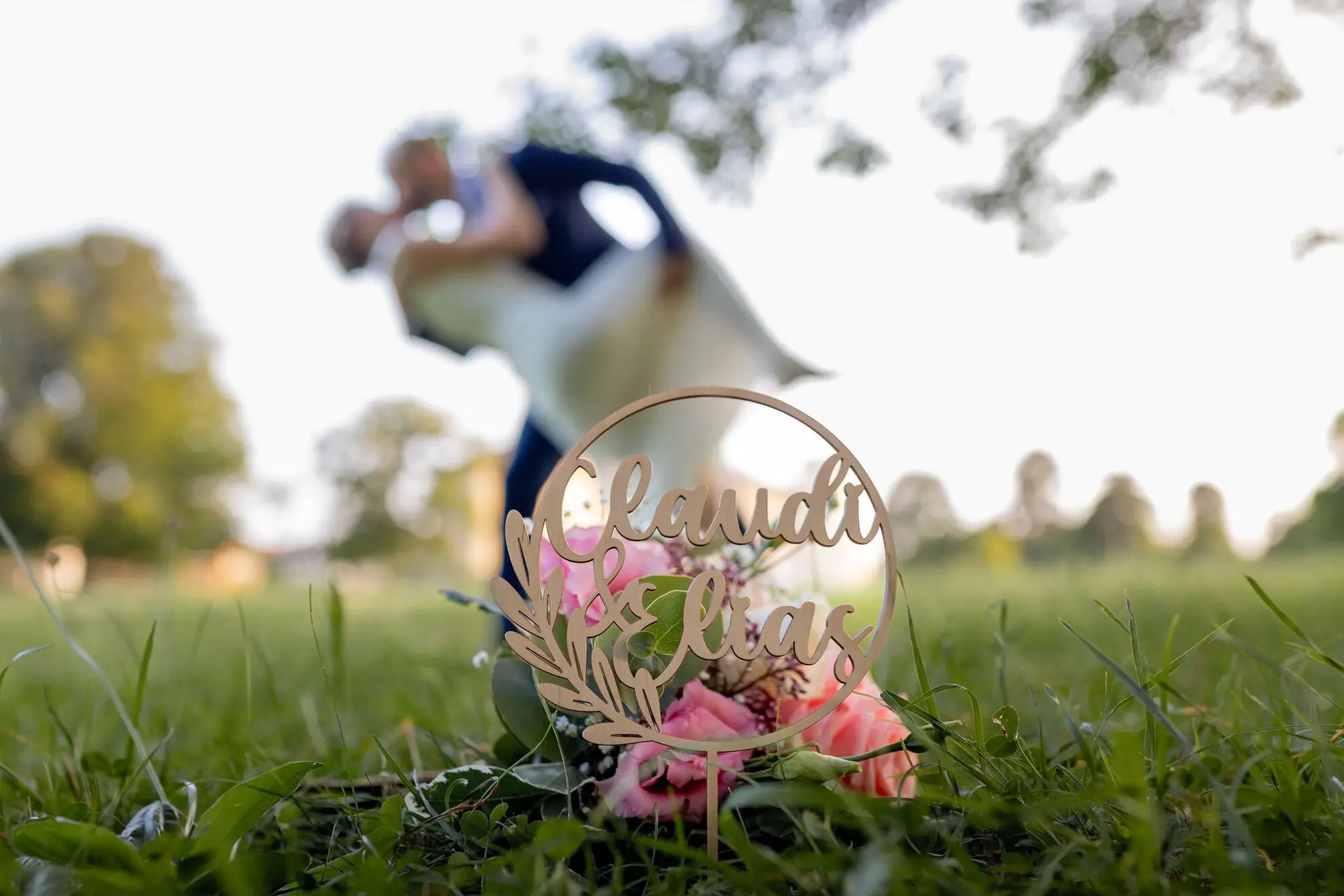 Brautpaar liegt in romantischer Umarmung auf einer Wiese, Bäume im Hintergrund unscharf
