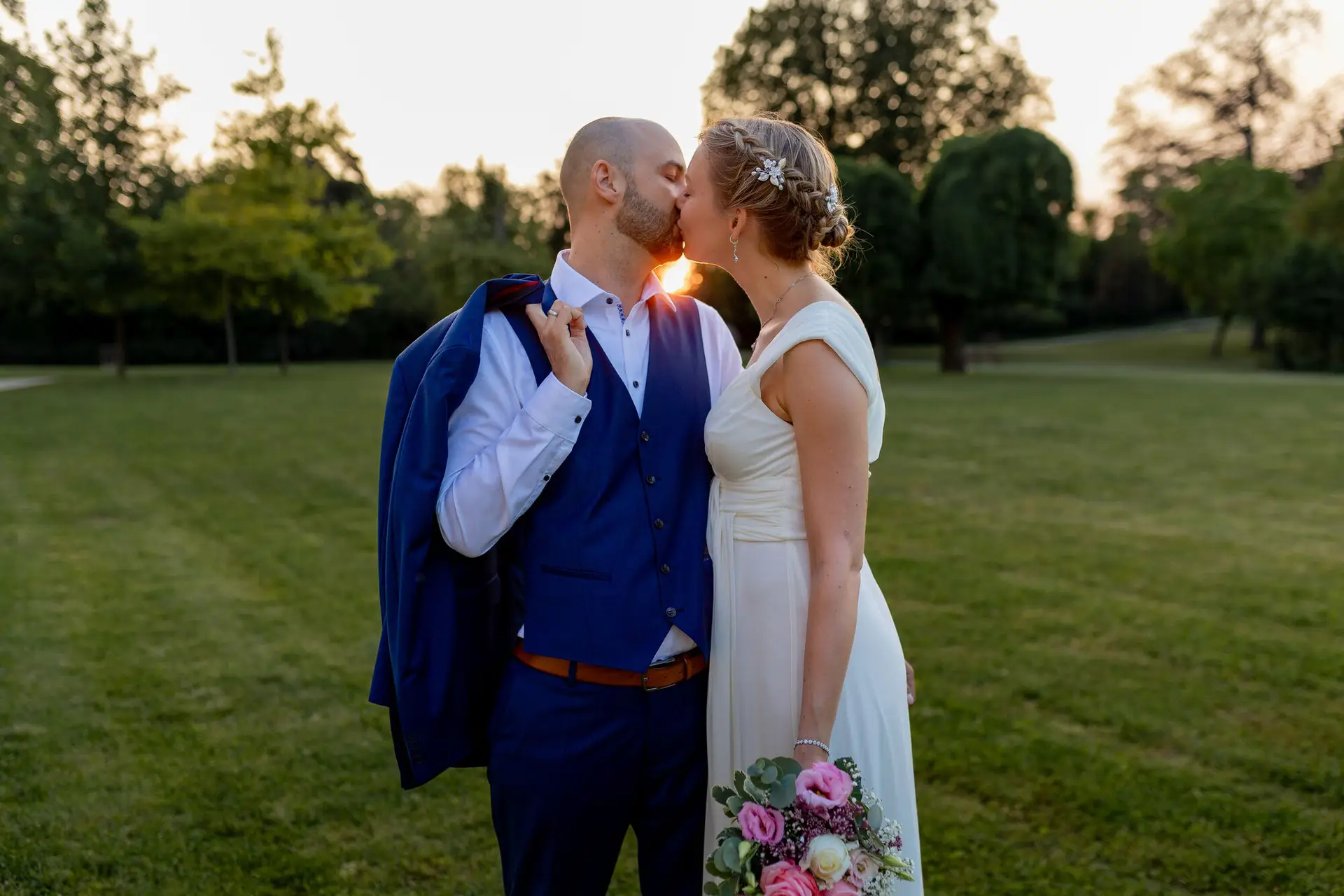 Brautpaar küsst sich auf einer Wiese im goldenen Sonnenuntergangslicht des Schlossgartens Herrnsheim