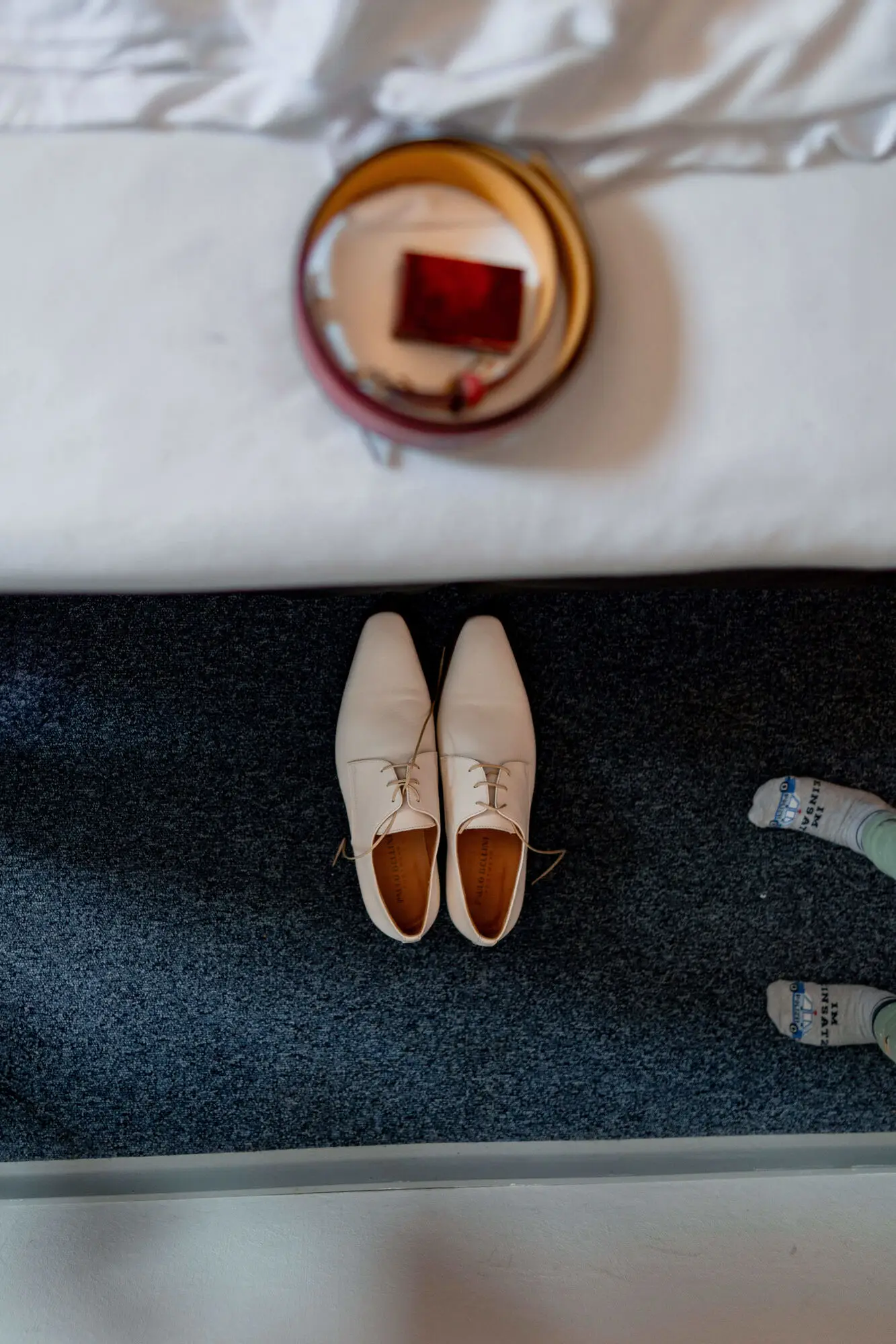 Elegante beige Bräutigam-Schuhe mit braunen Details auf dunklem Hotelteppich