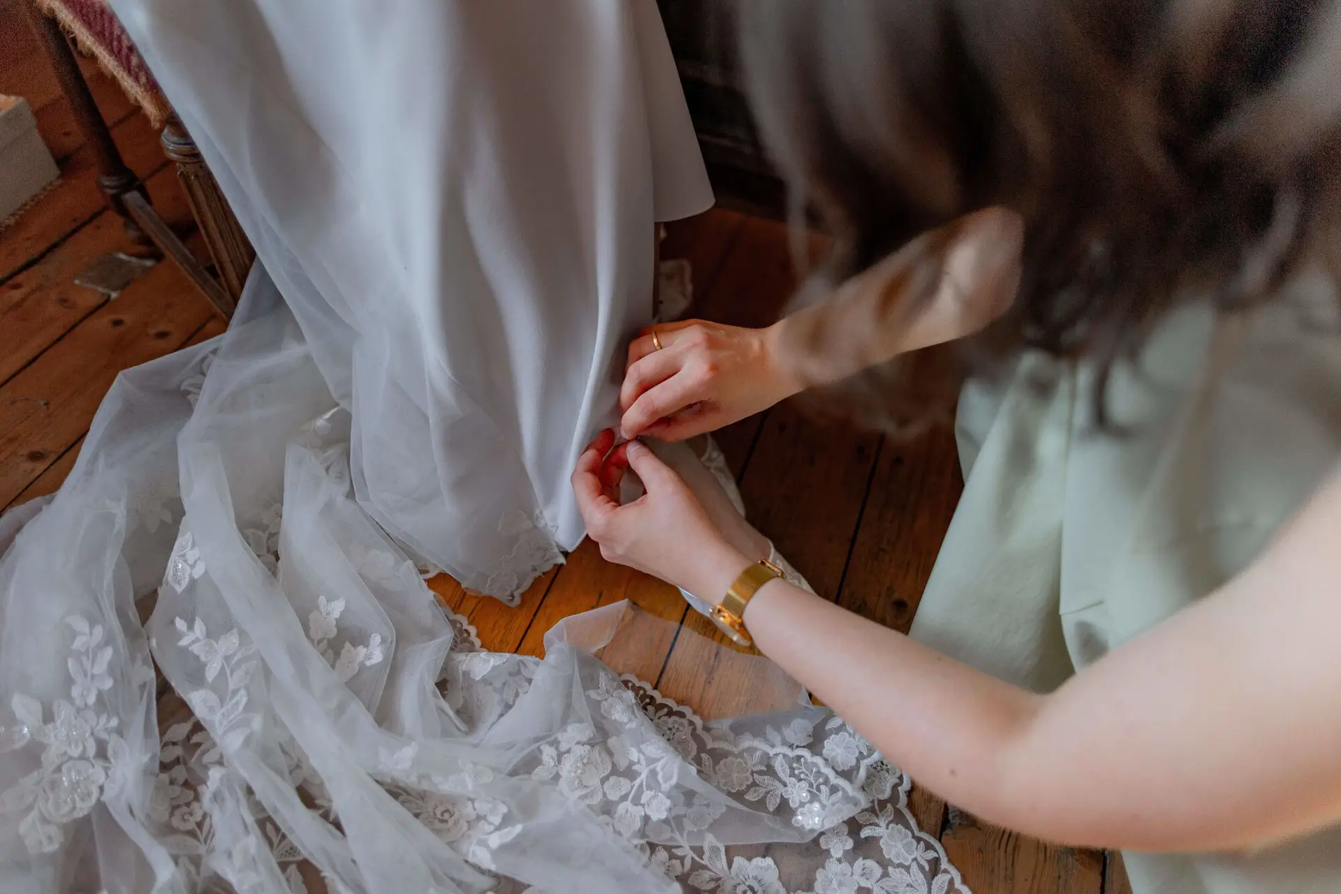 Trauzeugin befestigt den Saum des Brautkleids auf dem Holzboden