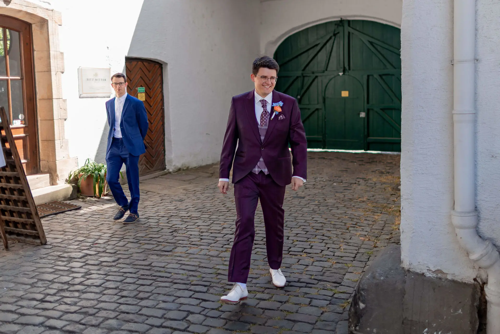 Bräutigam im bordeaux Hochzeitsanzug betritt den Innenhof zum First Look