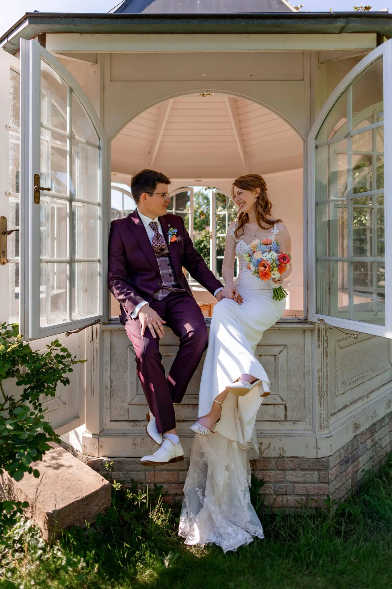 Brautpaar sitzt entspannt auf Pavillon-Bank im sonnigen Garten