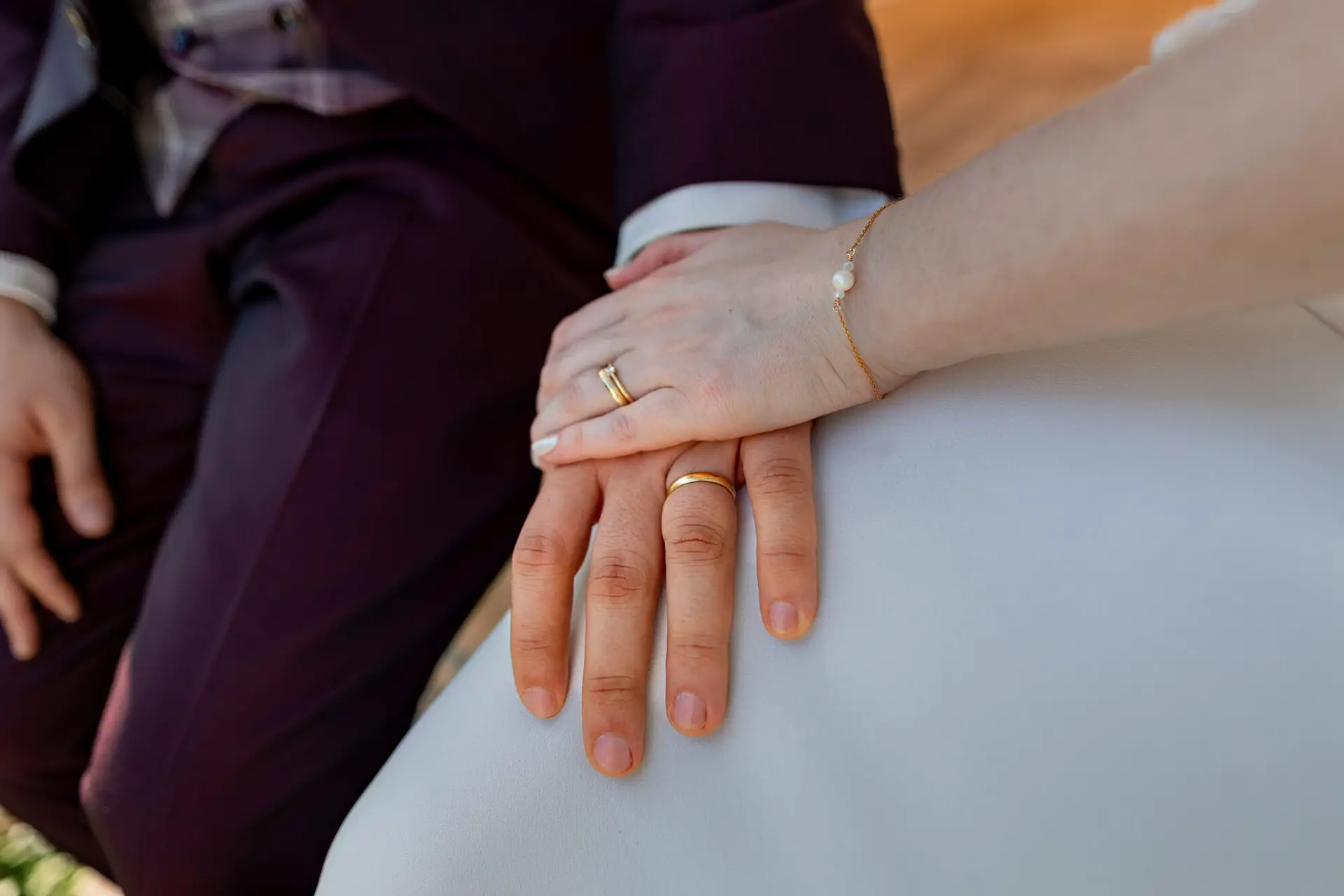 Detailaufnahme goldener Eheringe und Perlenarmband auf den Händen der Braut