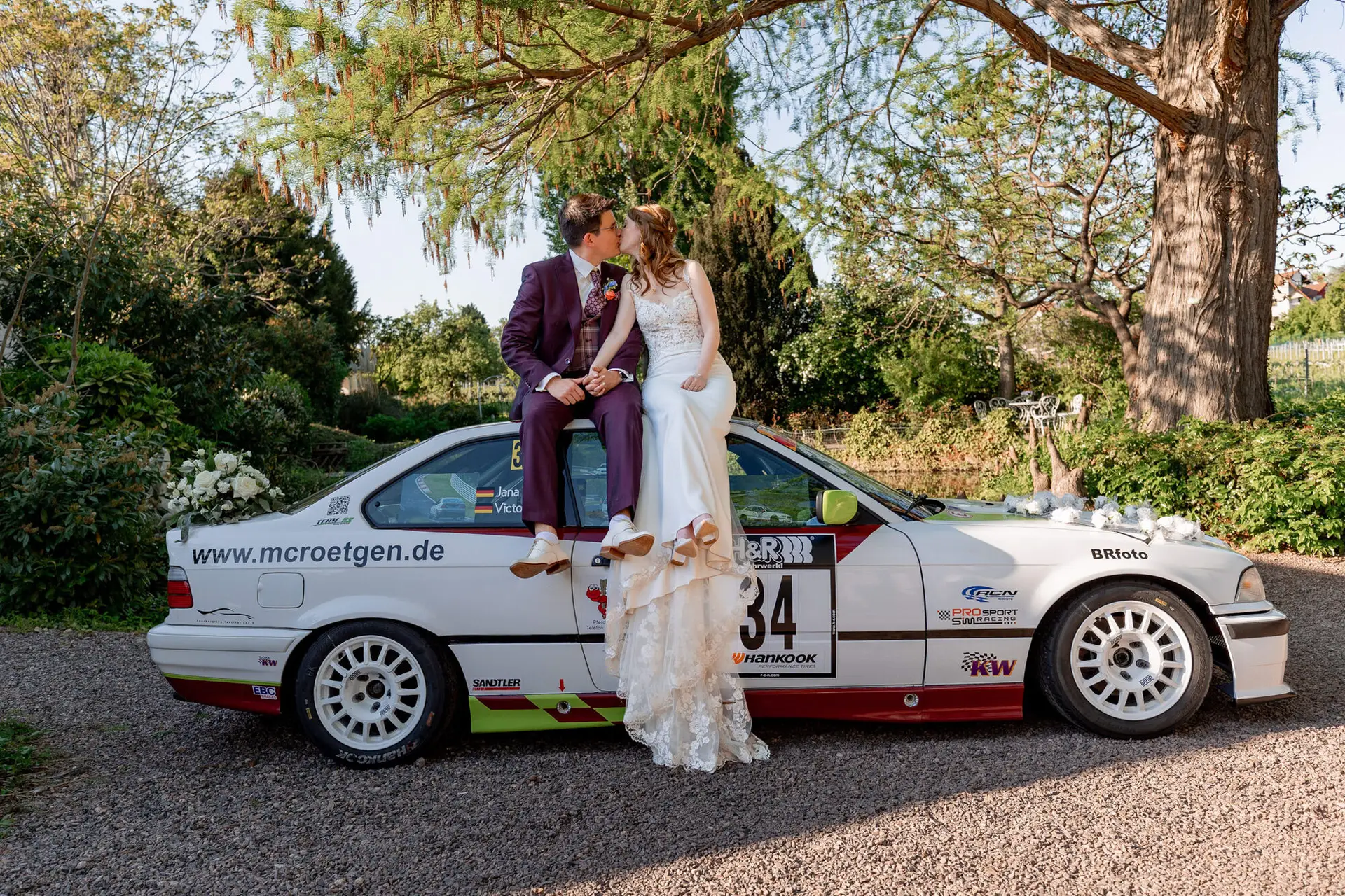 Brautpaar küsst sich auf der Motorhaube des Rallyeautos im Weinberg