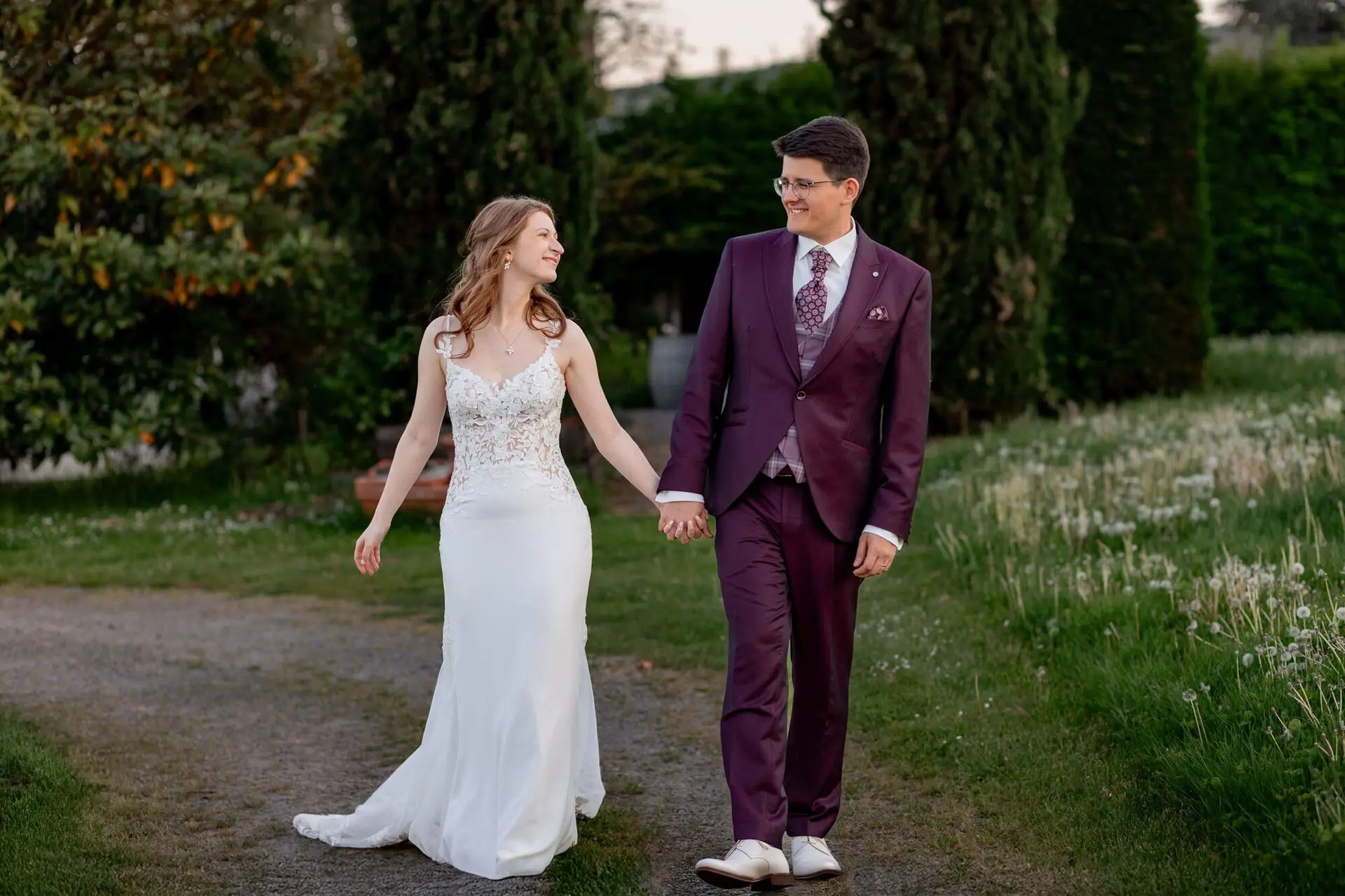 Brautpaar läuft Hand in Hand auf Kiesweg im abendlichen Gutspark