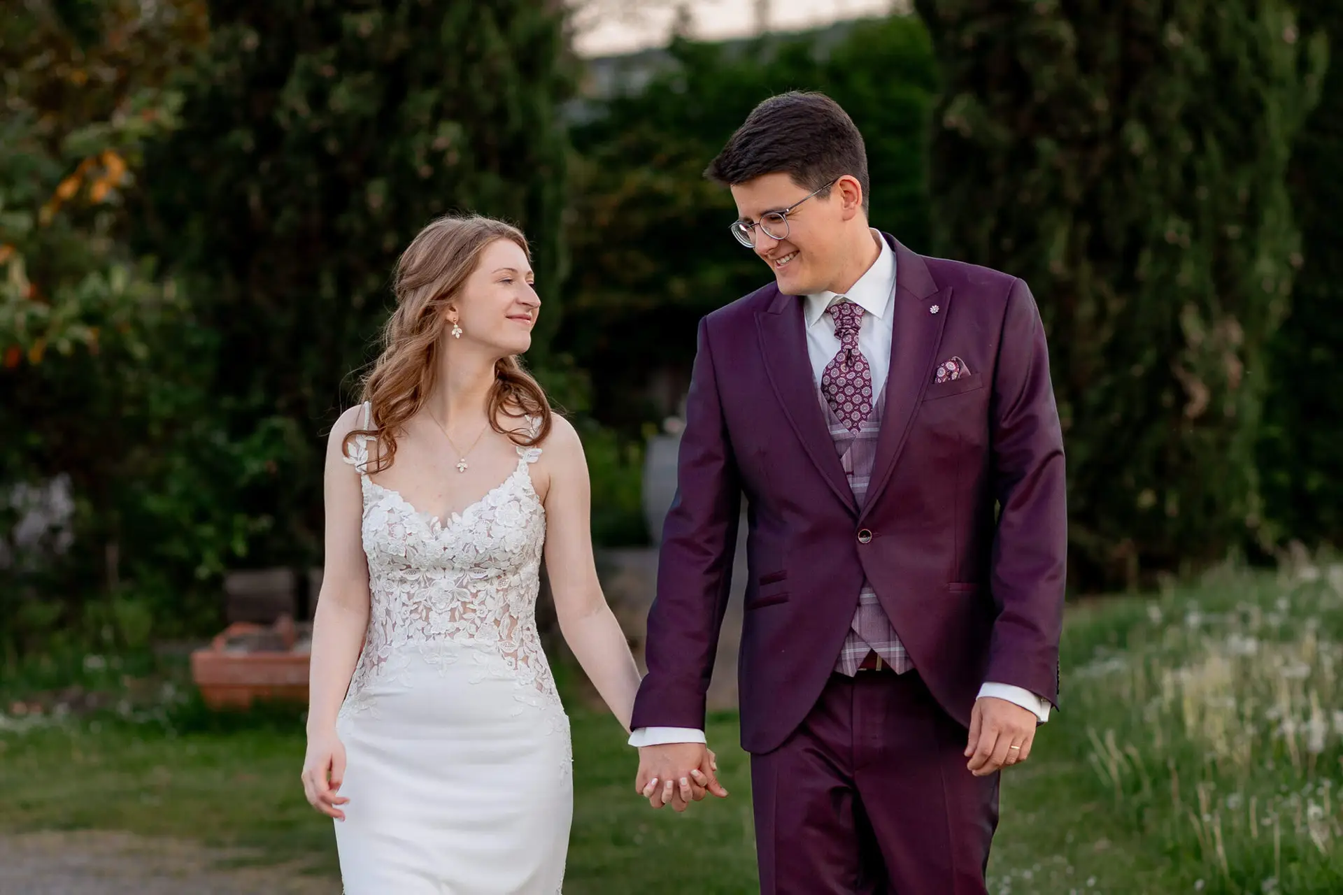 Brautpaar spaziert Hand in Hand mit Blick auf die Weinberge im Abendlicht