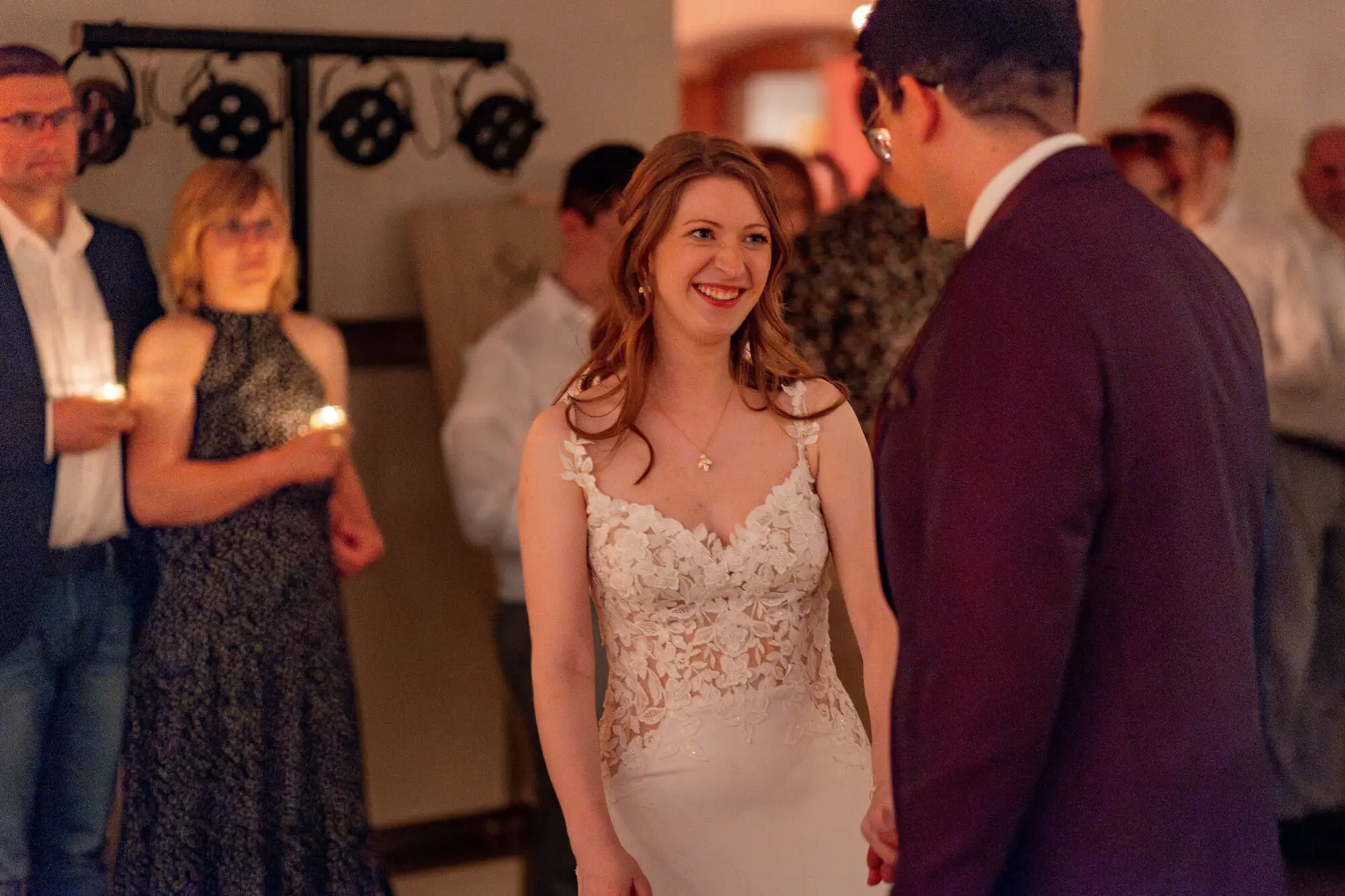 Strahlende Braut lächelt verliebt vor dem Bräutigam im Festsaal