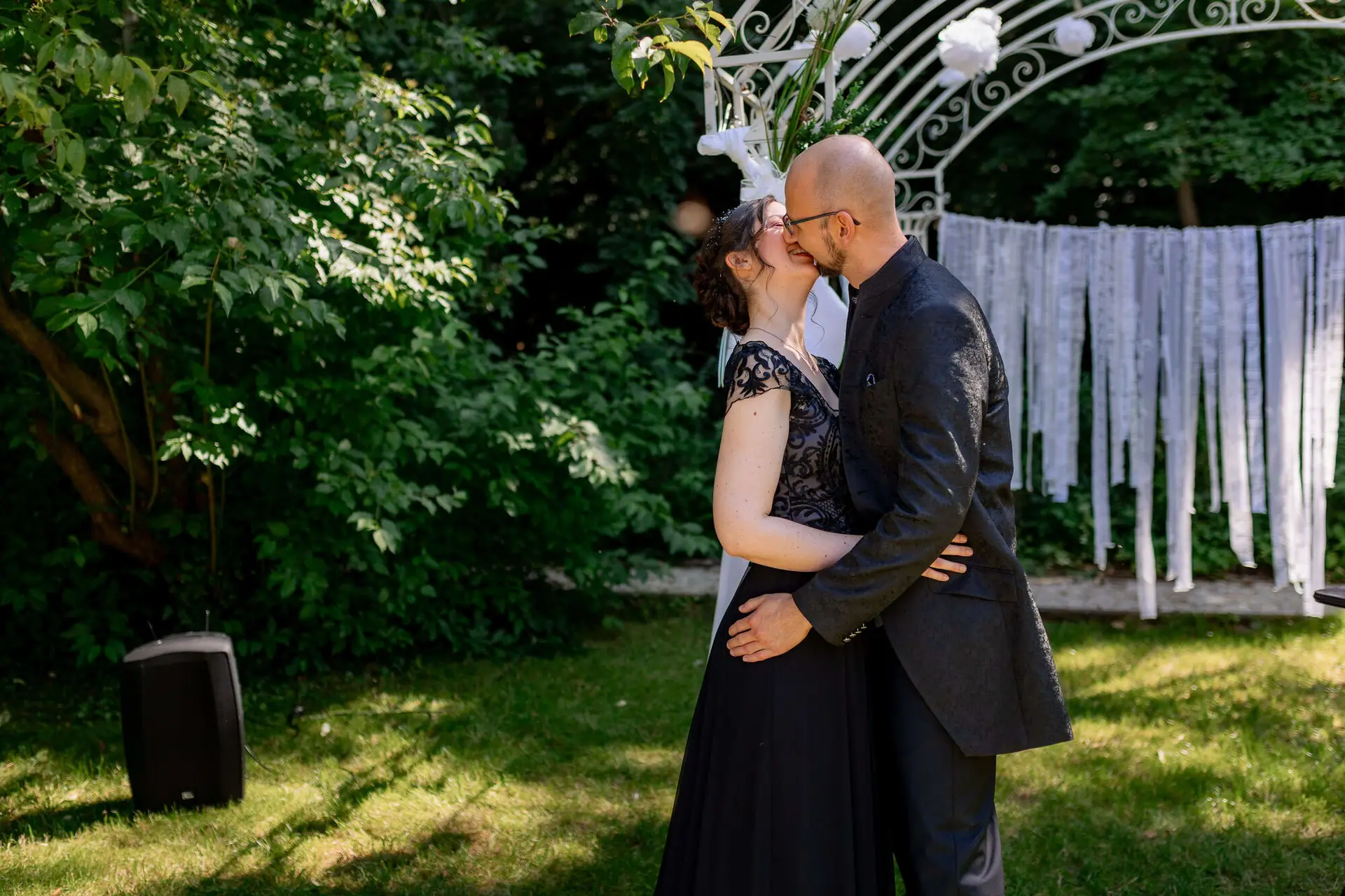 Brautpaar unter dem weißen Traubogen umgeben von Gästen