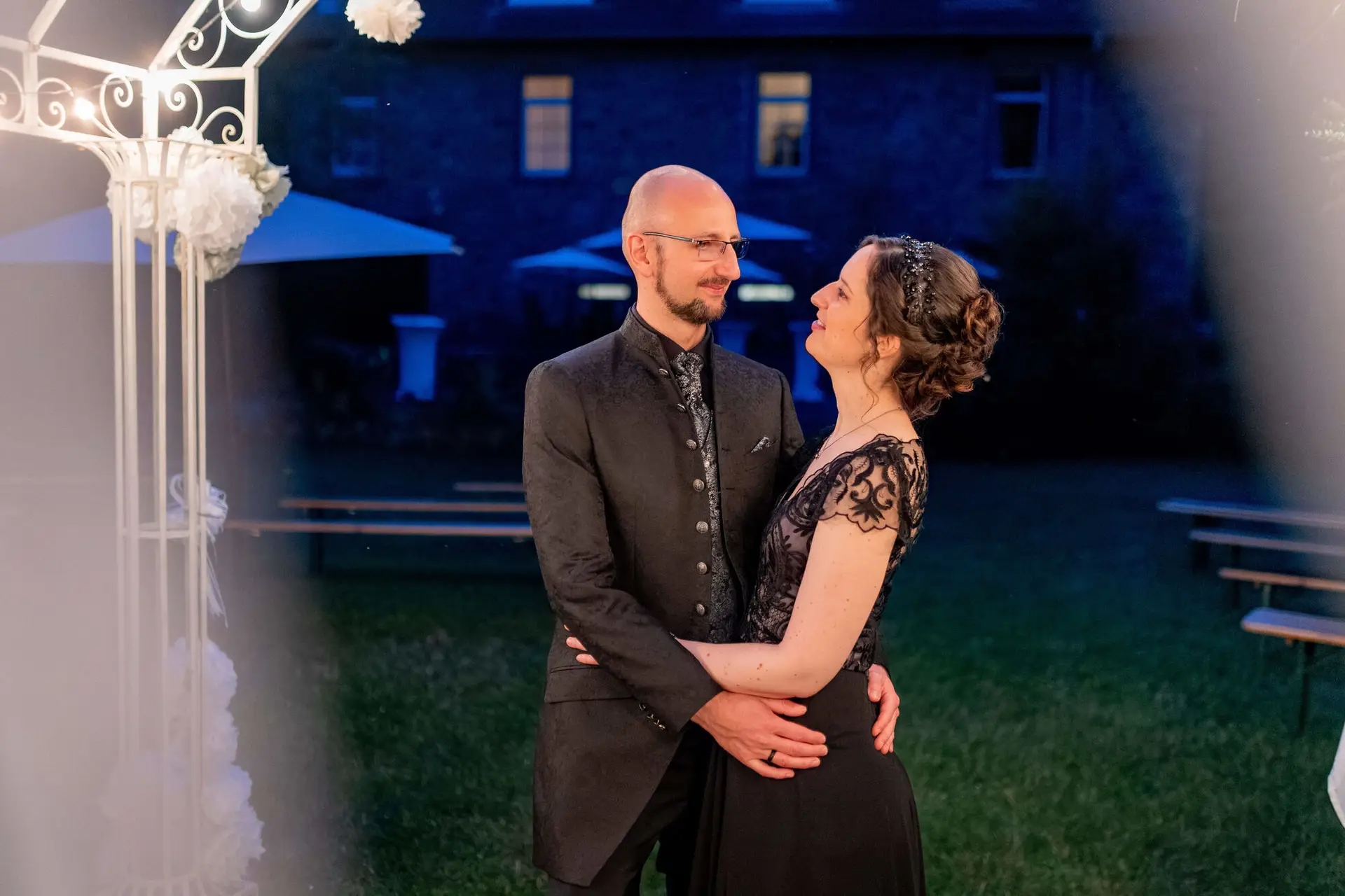 Grün beleuchteter Innenhof mit Hochzeitstafeln und Holzstühlen