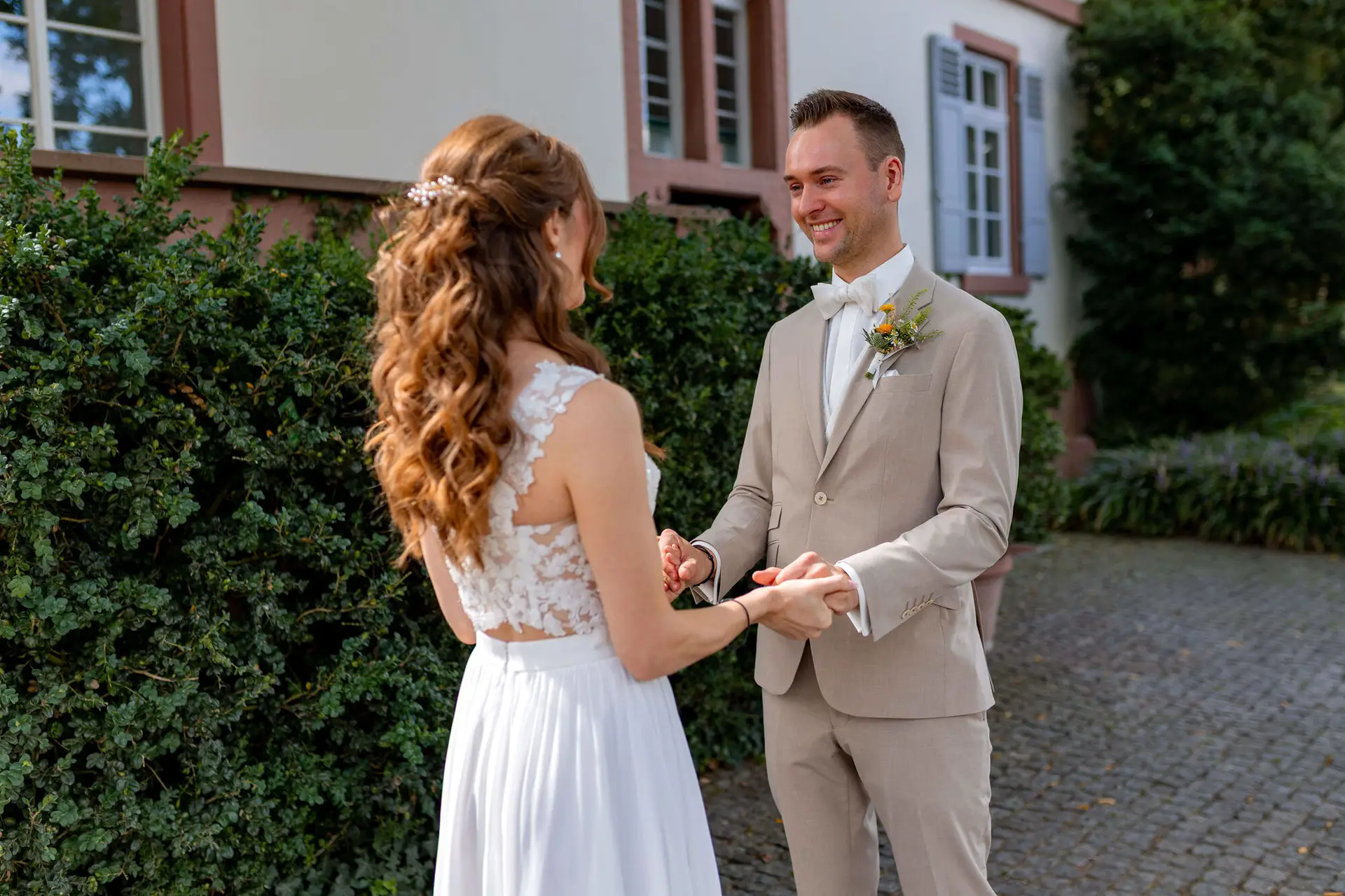 Bräutigam lächelt die Braut beim First Look an und hält ihre Hand