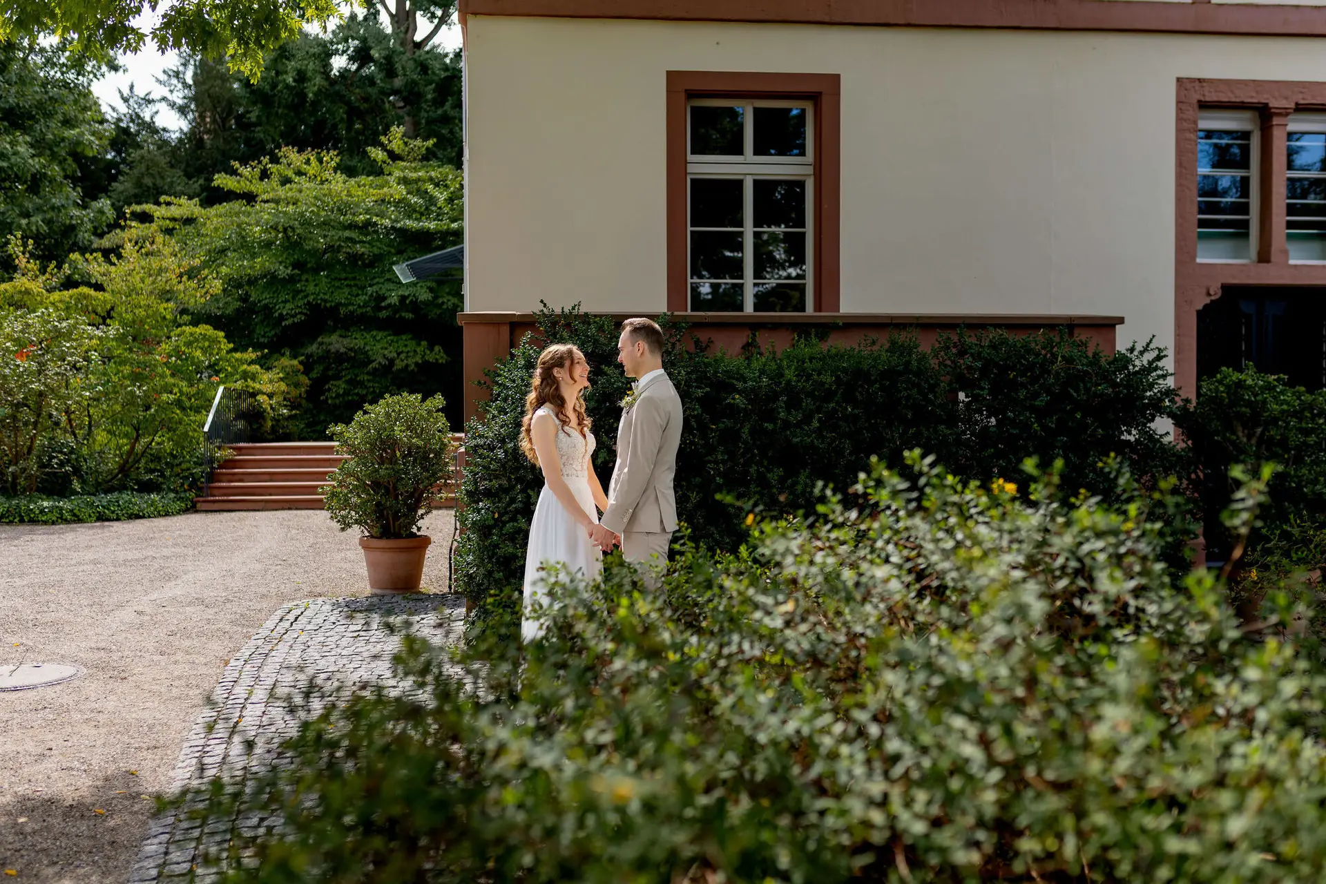 Brautpaar steht sich gegenüber vor historischem Gebäude mit Hecke