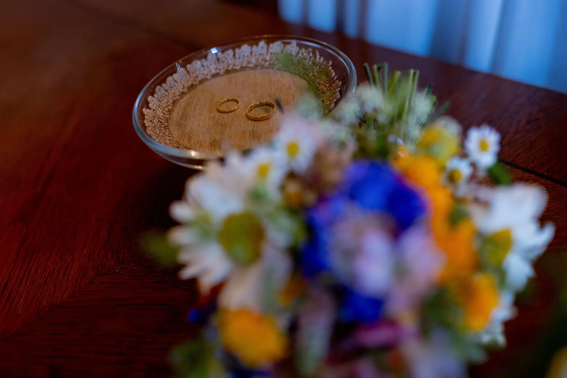 Eheringe auf einem Ringkissen neben buntem Brautstrauß