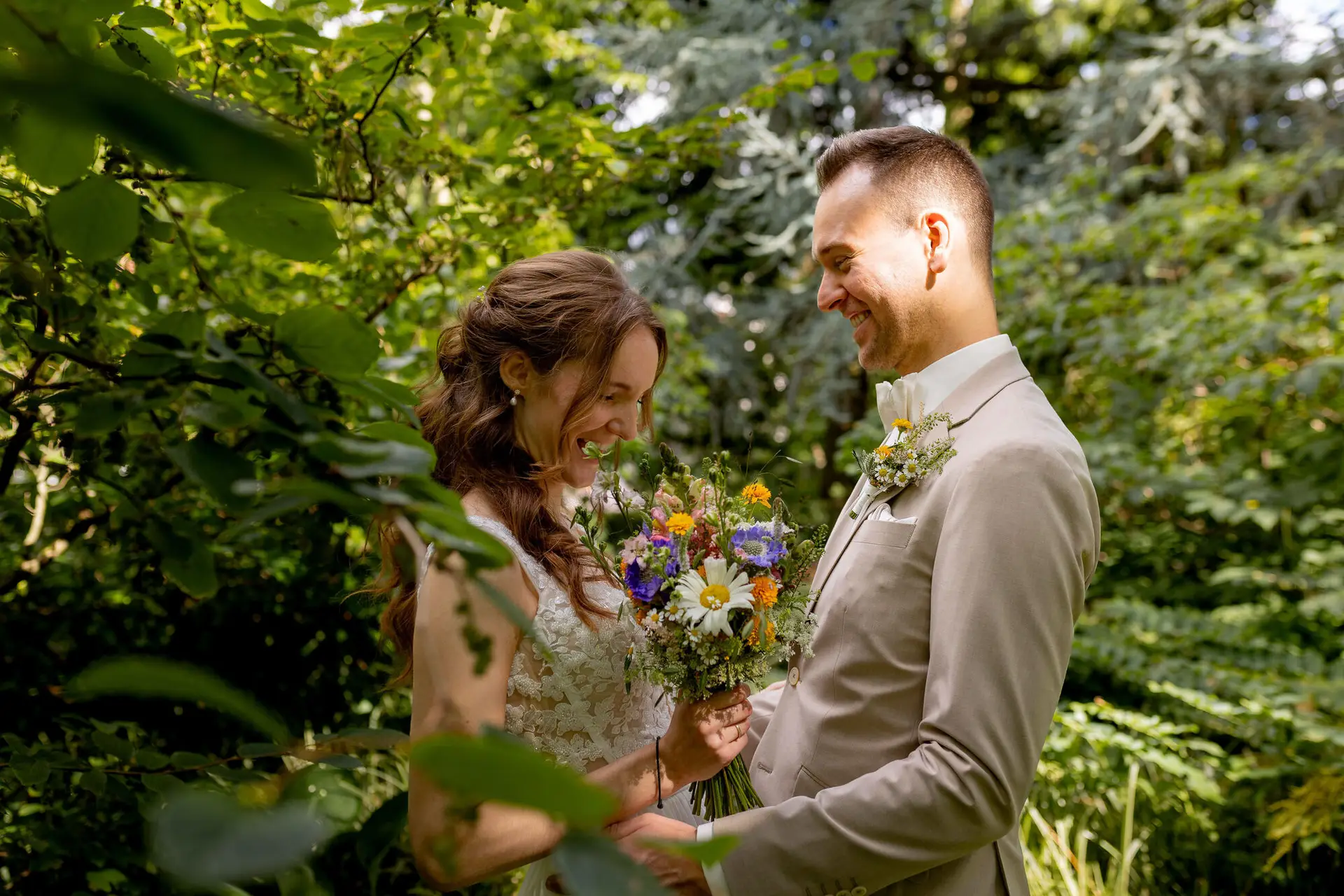 Brautpaar lacht sich an zwischen grünem Blattwerk im Hermannshof
