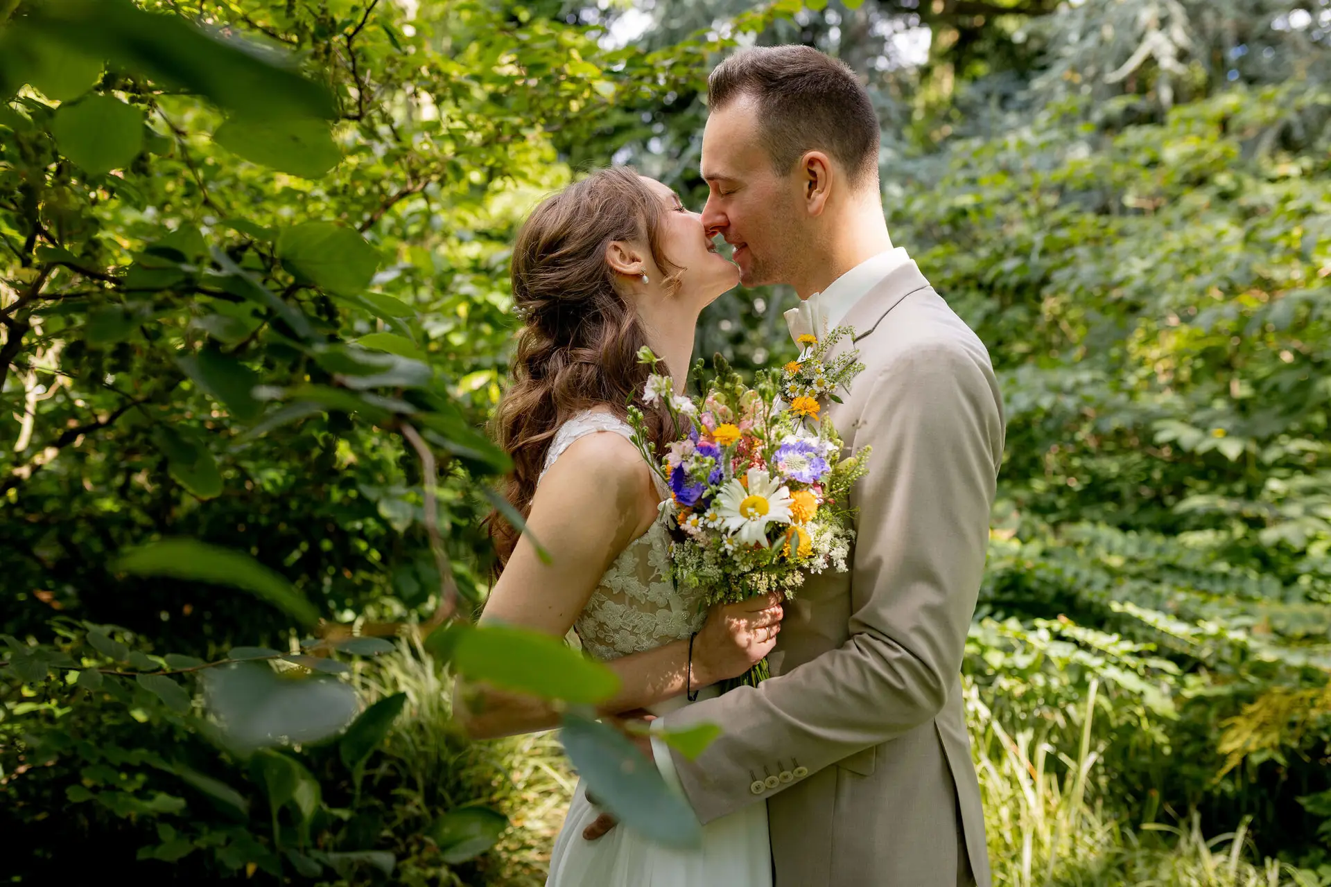 Brautpaar küsst sich umgeben von üppigem Grün im Hermannshof