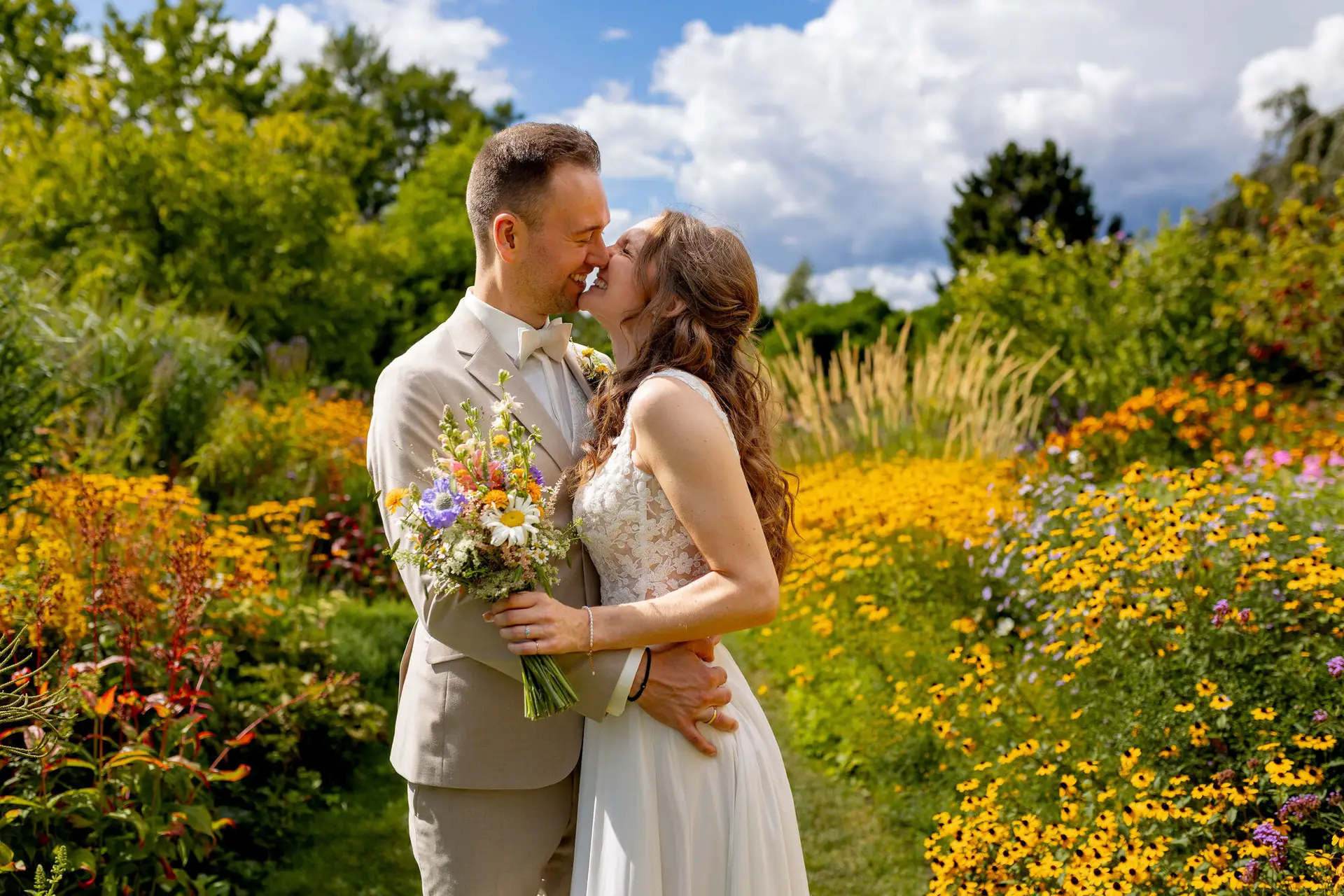 Brautpaar küsst sich zwischen bunten Blumenbeeten im Hermannshof