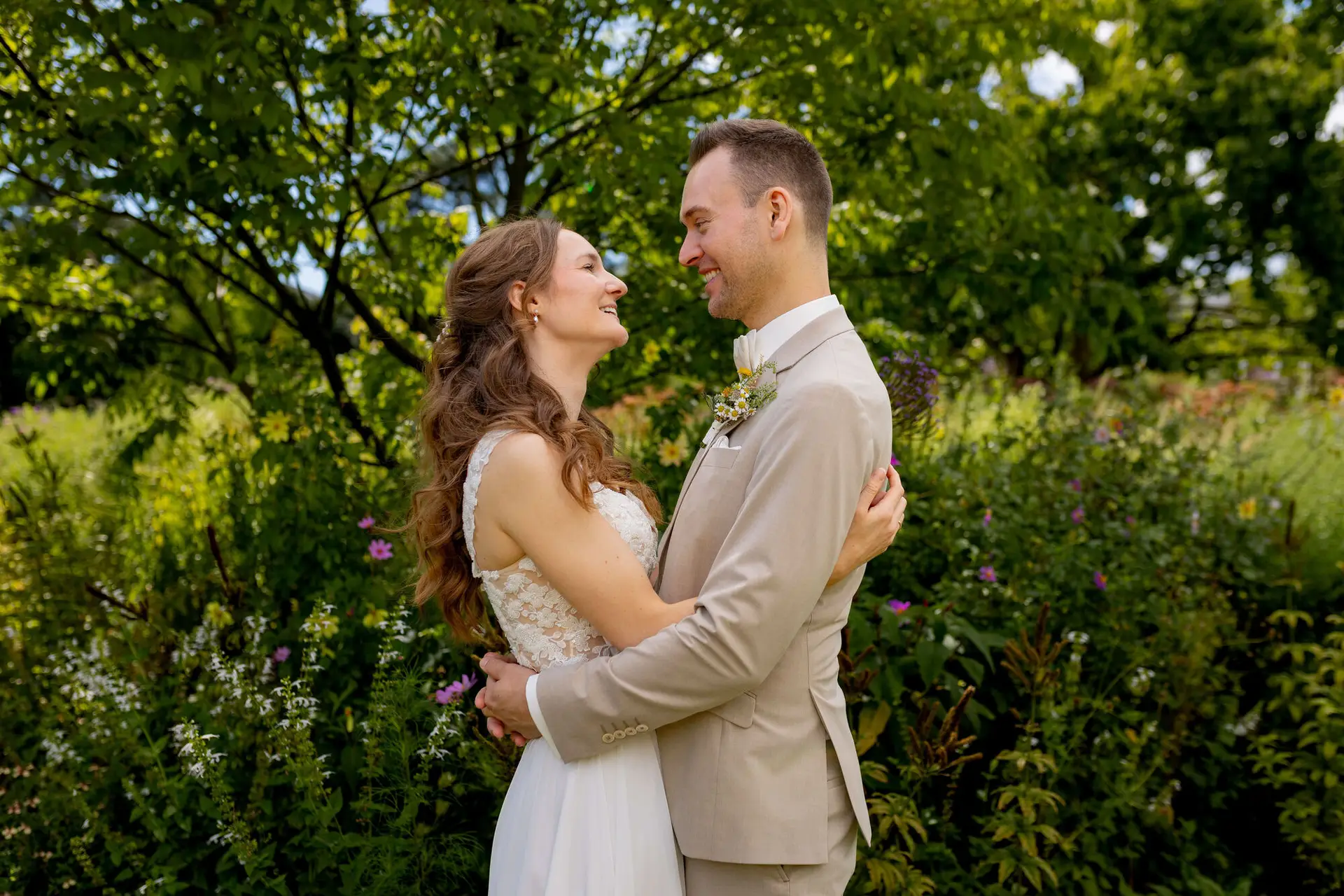 Brautpaar umarmt sich lächelnd vor grüner Gartenkulisse