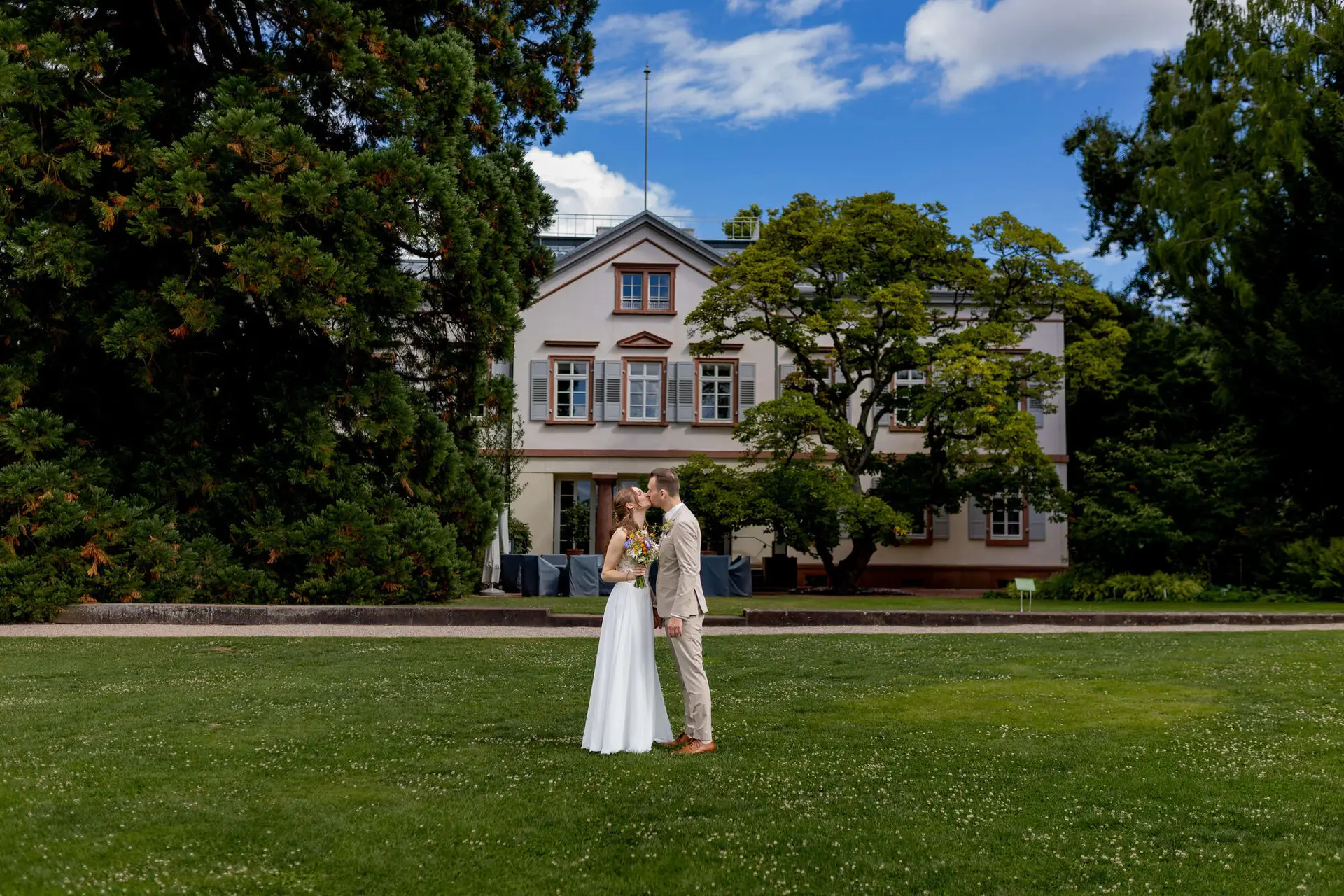Brautpaar küsst sich auf der Wiese vor dem Herrenhaus im Hermannshof