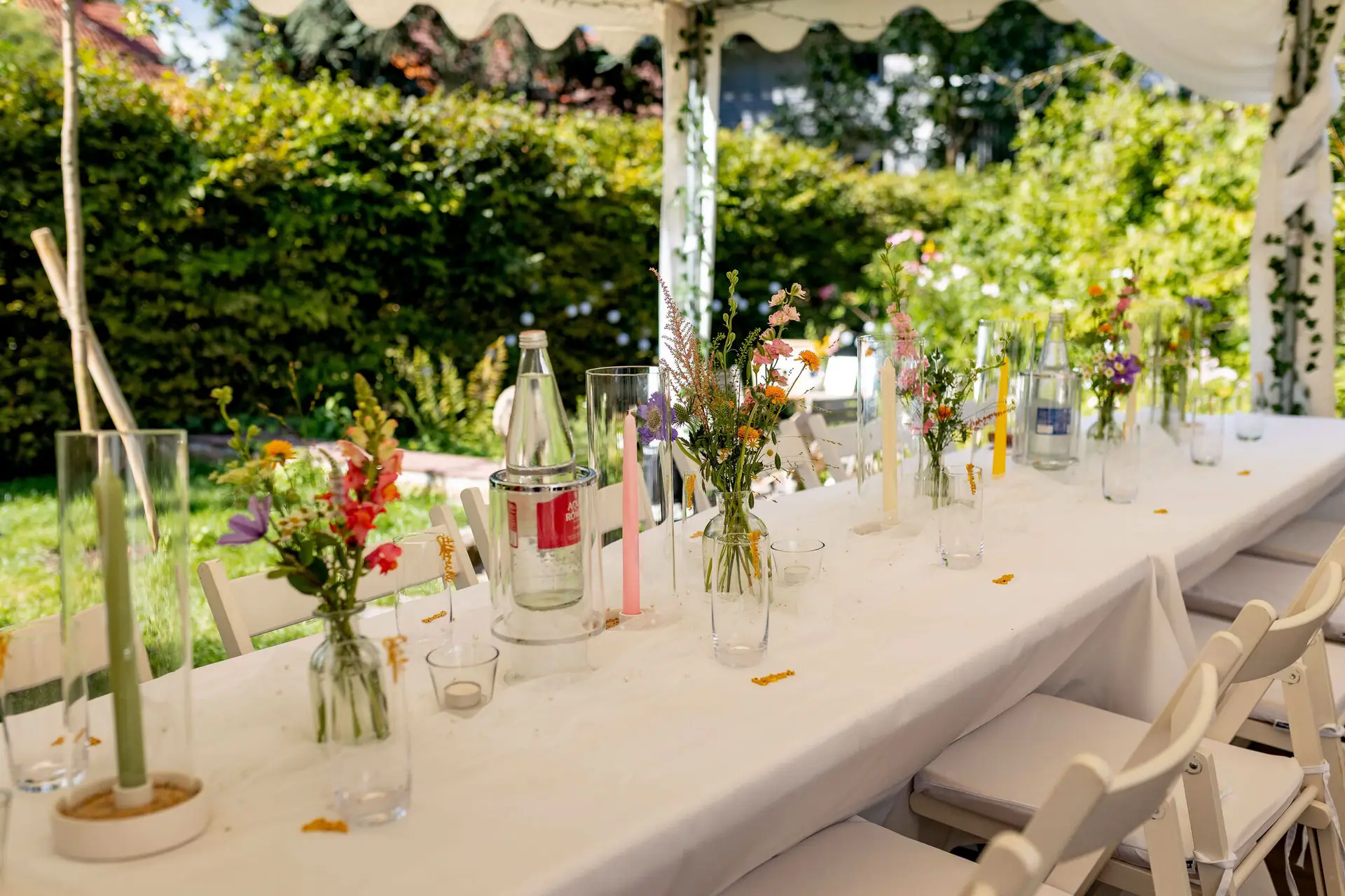 Dekorierter Hochzeitstisch mit Wildblumensträußen und rosa Kerzen unter dem Gartenzelt