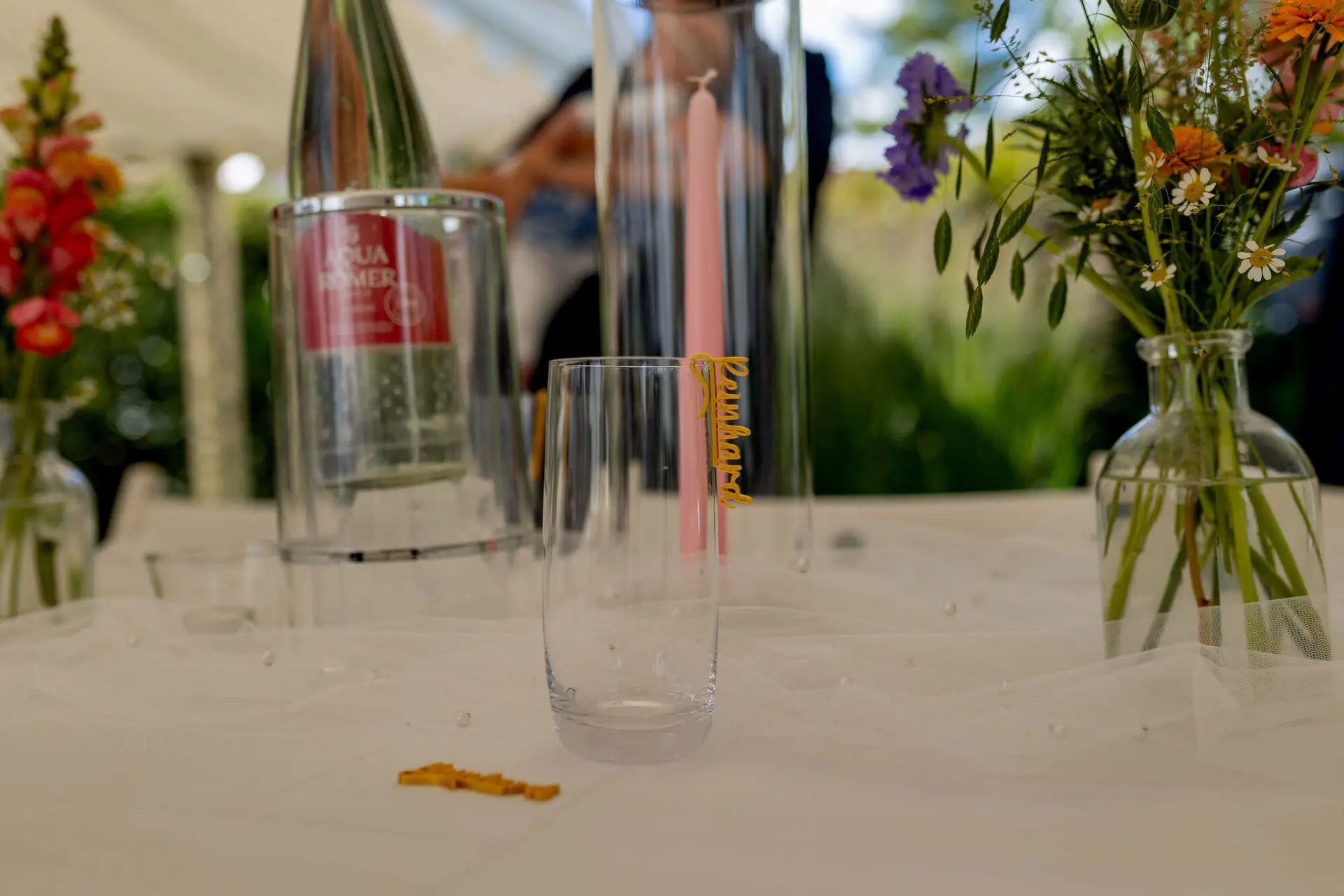 Trinkglas mit personalisiertem Namensschild neben Blumenvase auf dem Hochzeitstisch