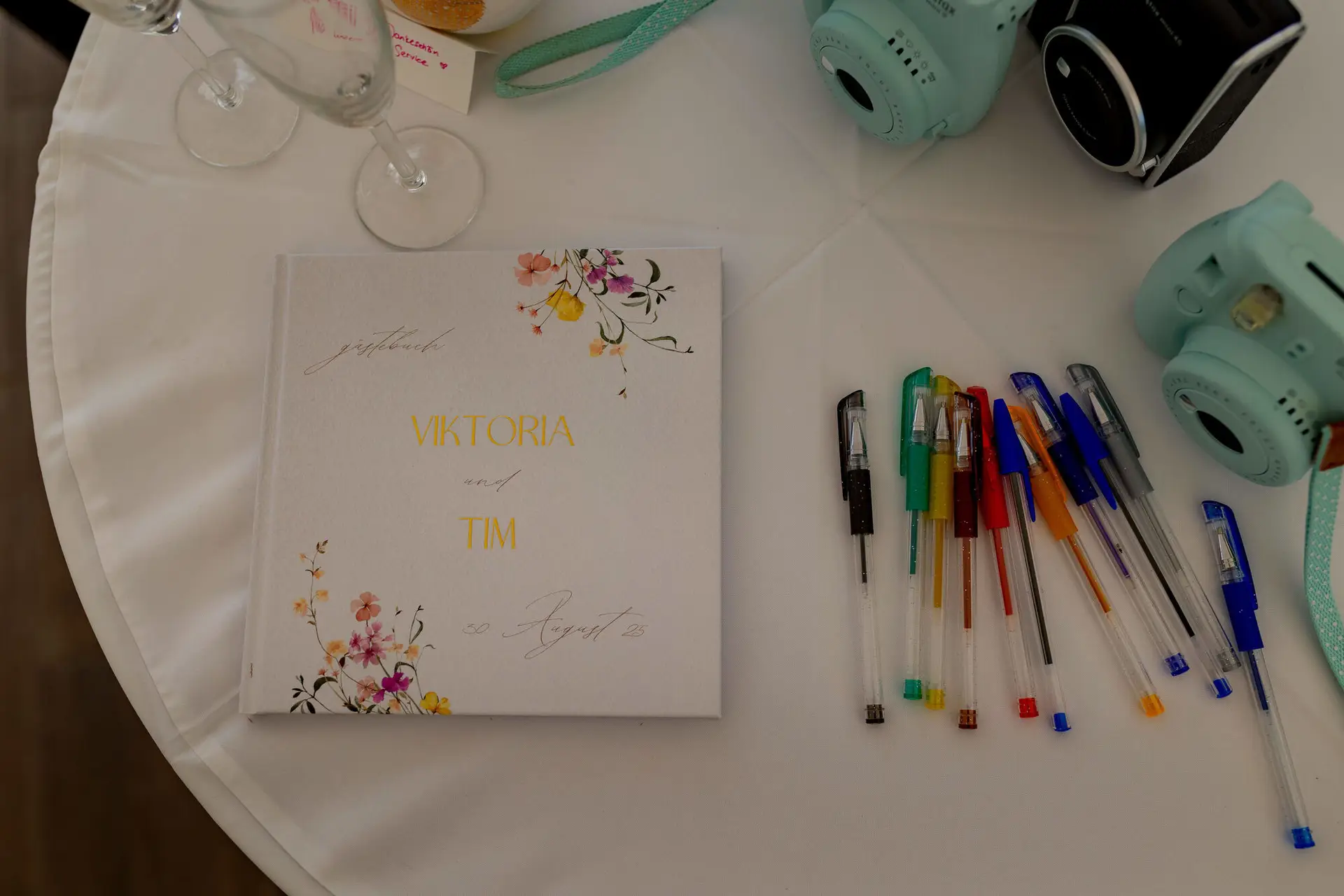 Gästebuch mit Aufschrift Viktoria und Tim neben Instax-Kameras und bunten Stiften