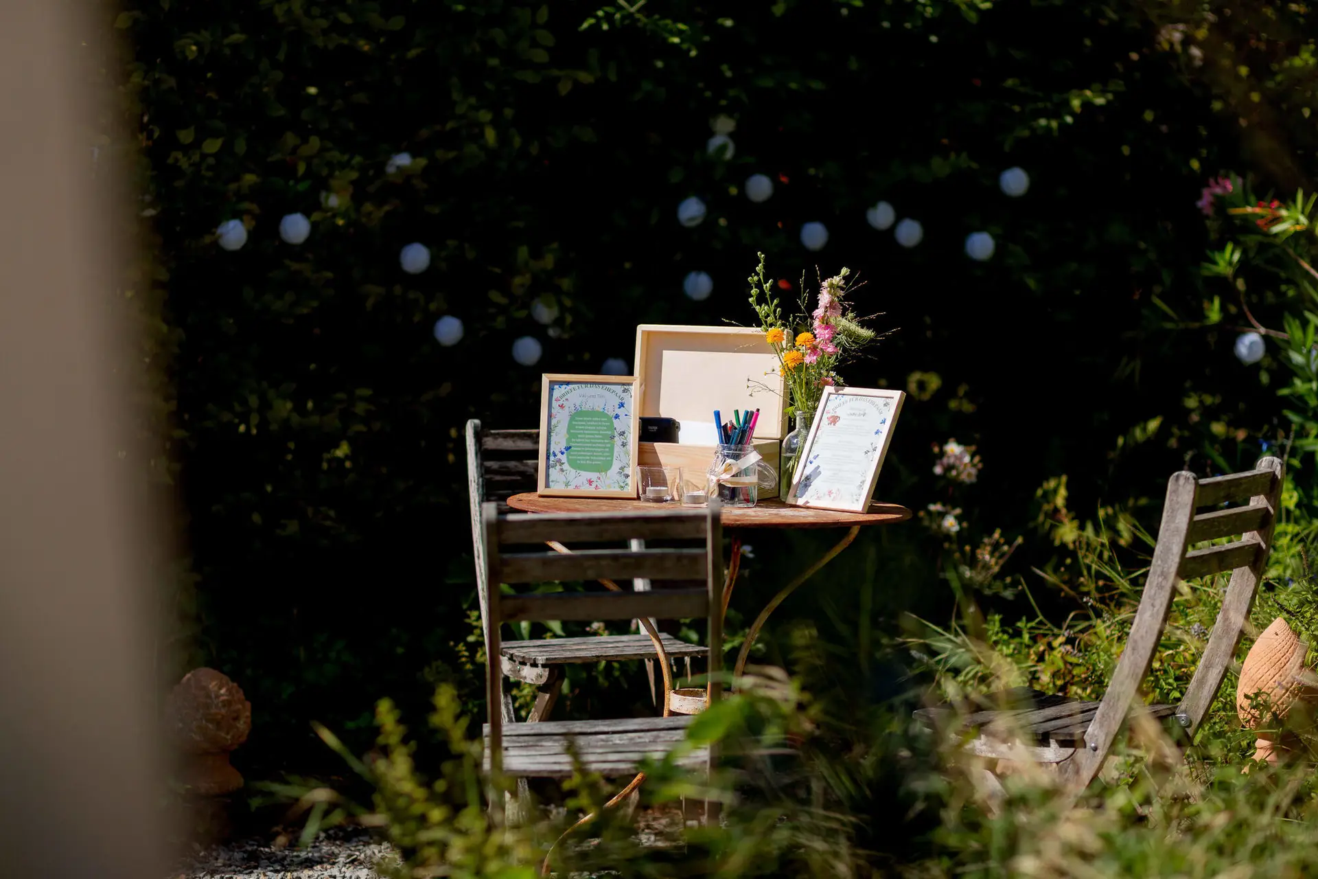 Kleiner Holztisch mit Bilderrahmen, Stiften und Blumen im grünen Garten
